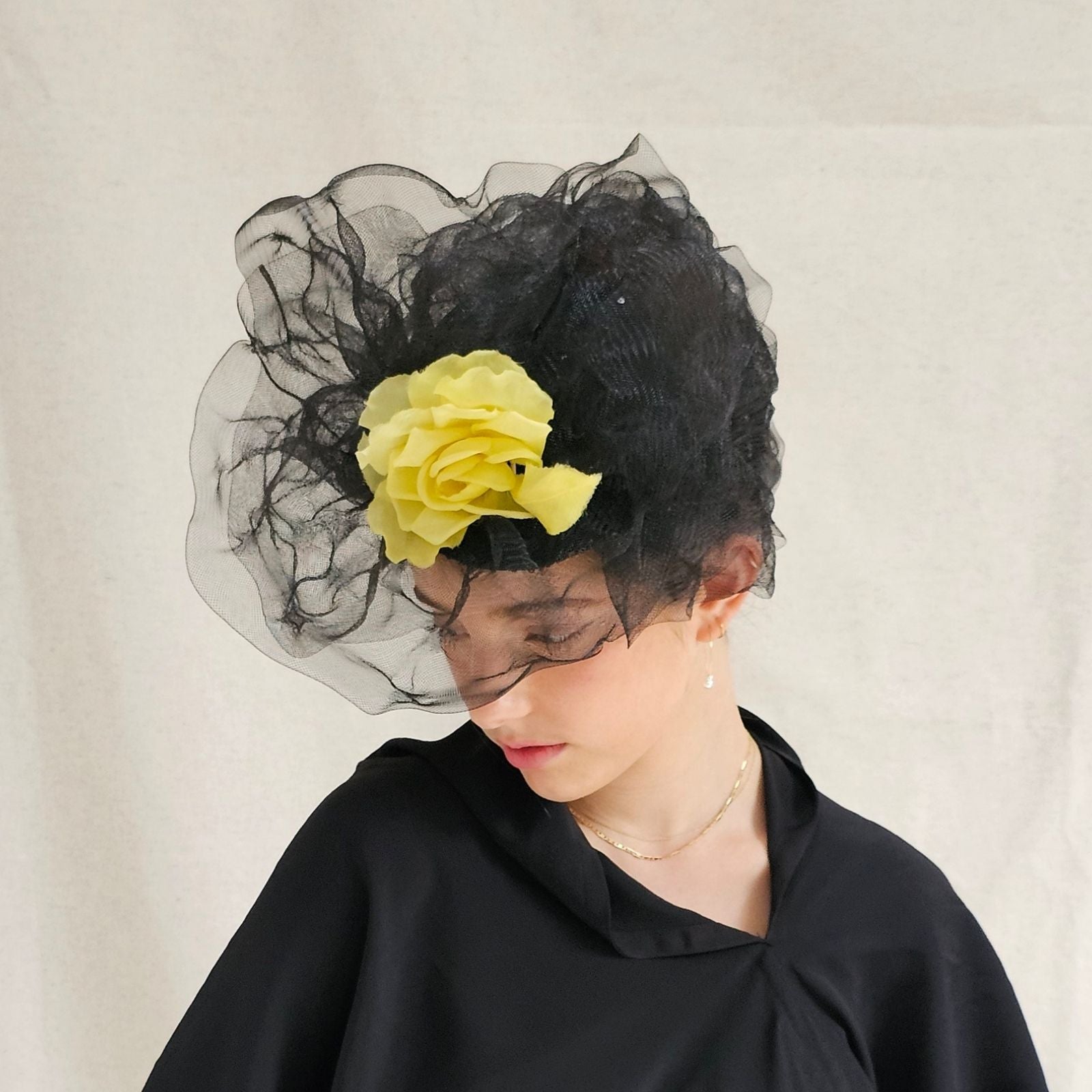 Black turban hat with dramatic crin swirl veiling and yellow flower embellishment, left view.