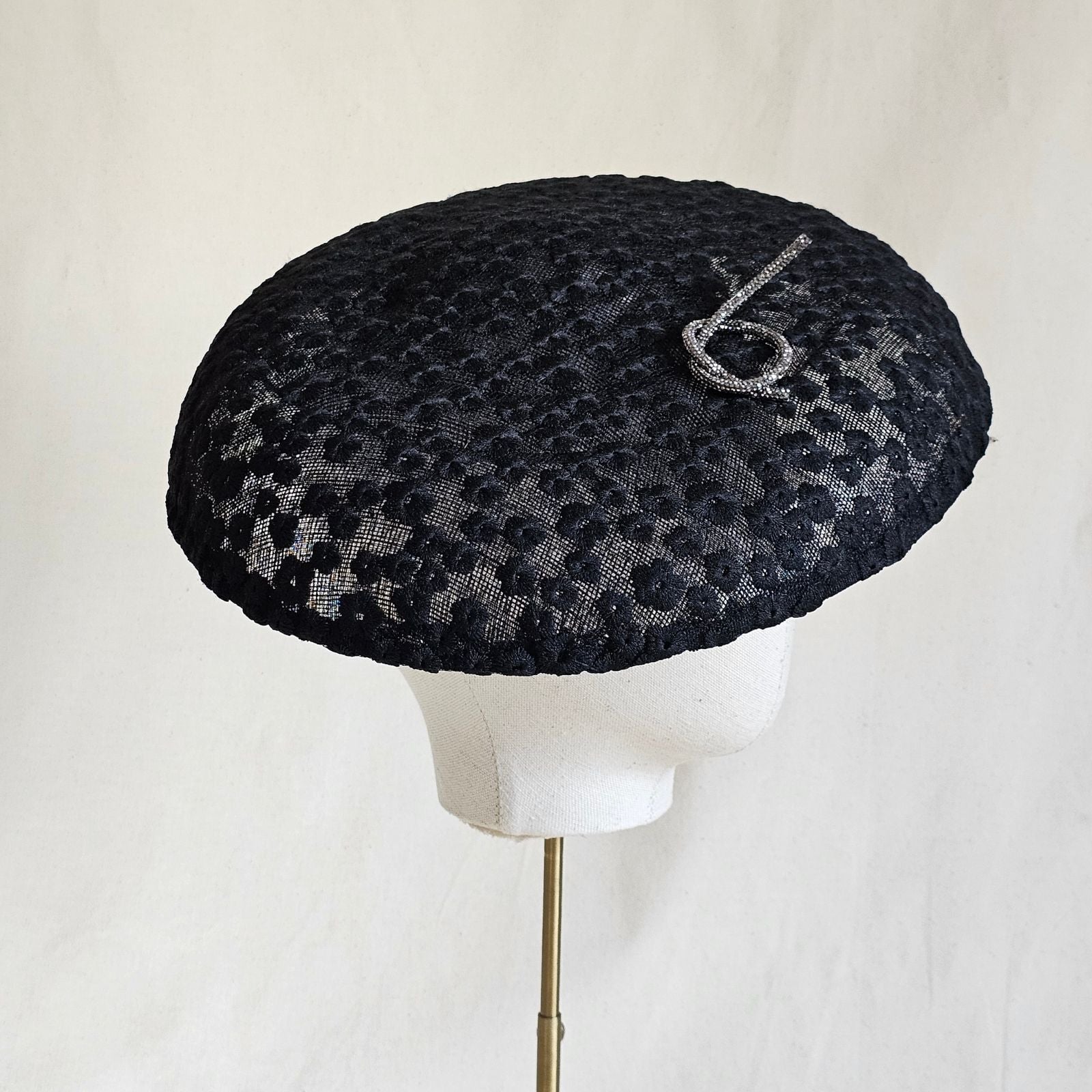 Black disc hat with beautiful flower lace and silver pretzel knot embellishment, side view.