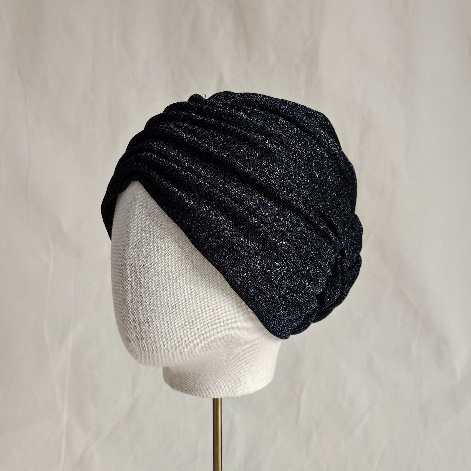 Black lurex turban loosely gathered into intricate plaited rose, left view.