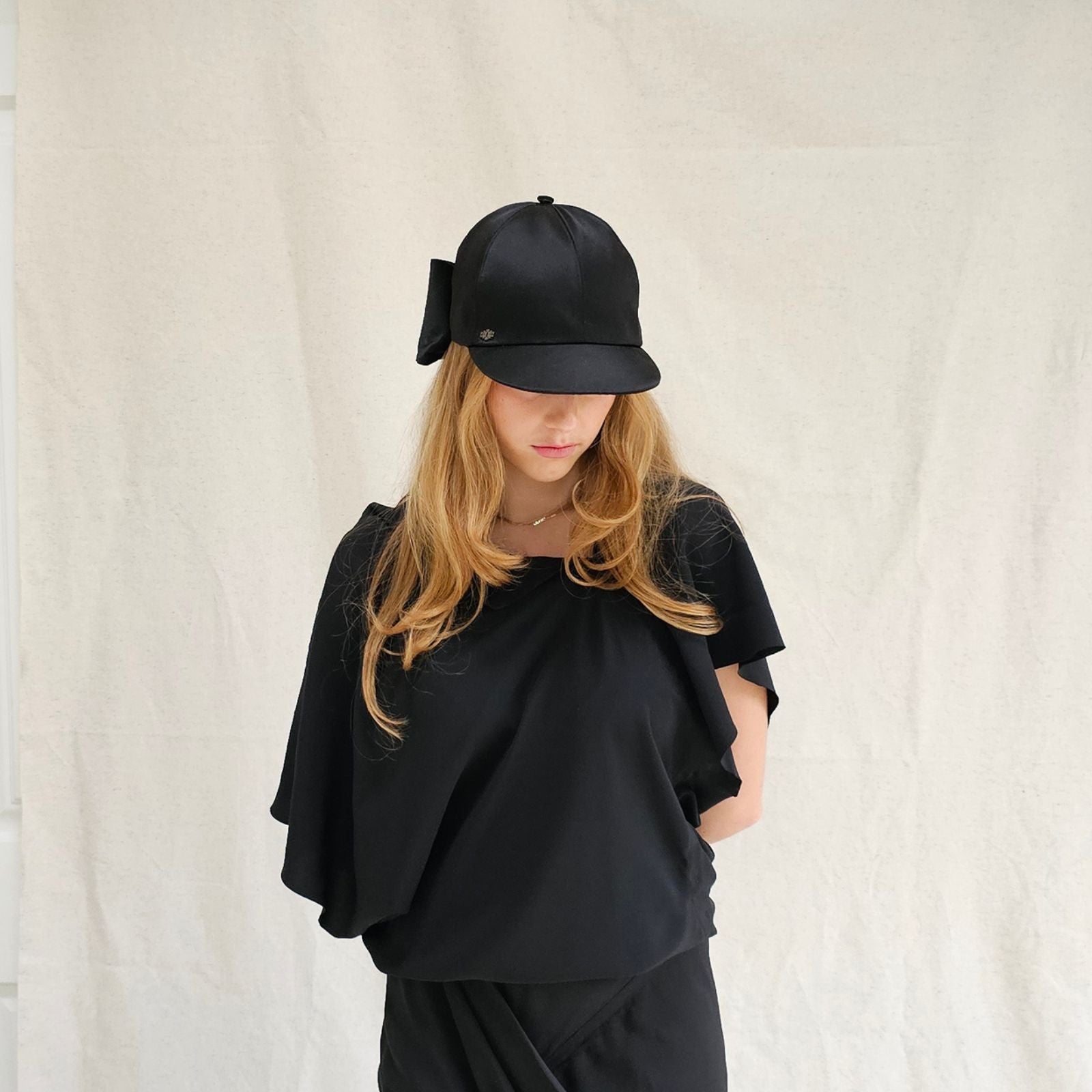 Black silk baseball cap with dramatic bow, front portrait view.