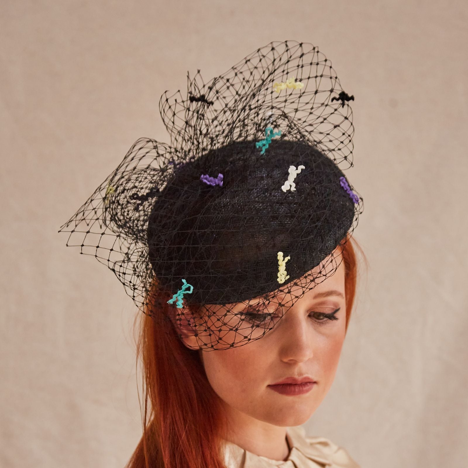 Black sinamay beret with intricate black veiling and multicolour bow detailing, front view.