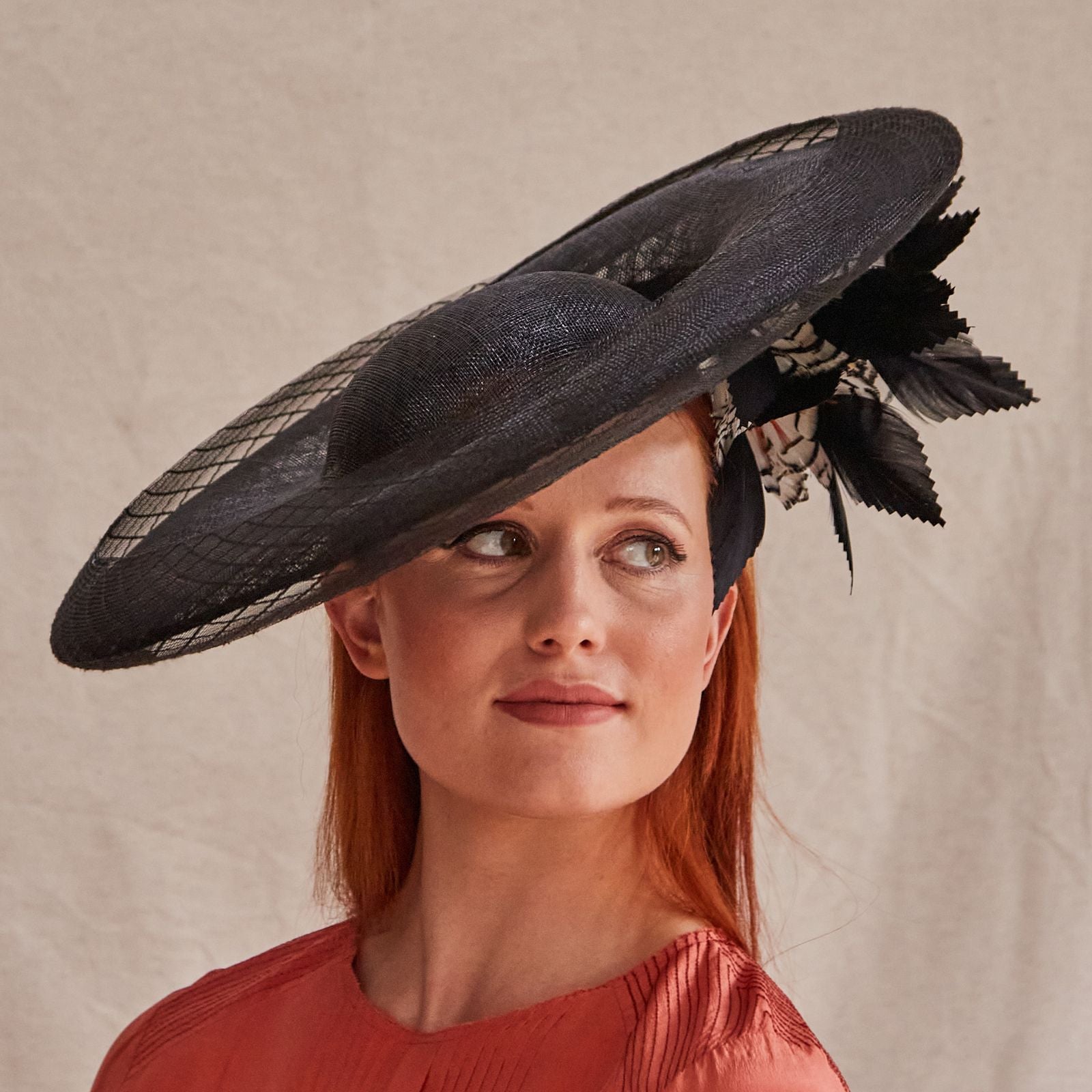 Black sinamay disc hat with crin embellishment and elegant underside feathers, angle view.
