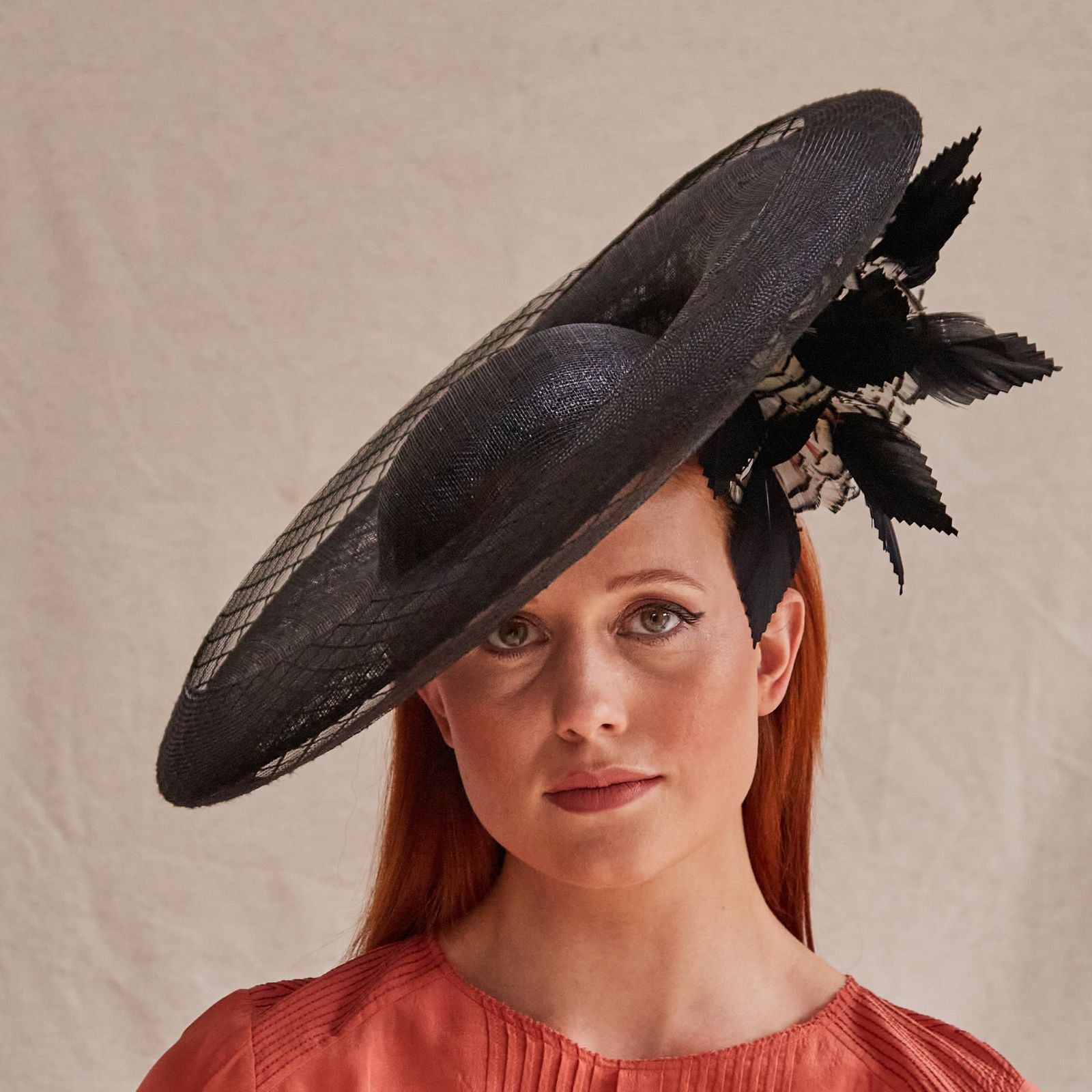 Black sinamay disc hat with crin embellishment and elegant underside feathers, front view.