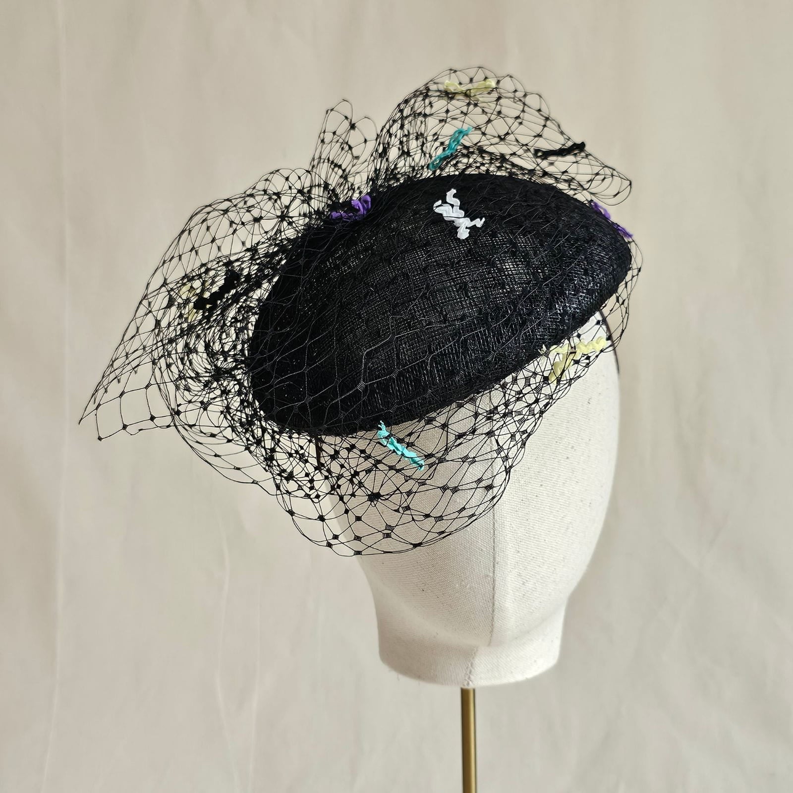 Black siname beret with veiling and multicolour bow detailing, front view.