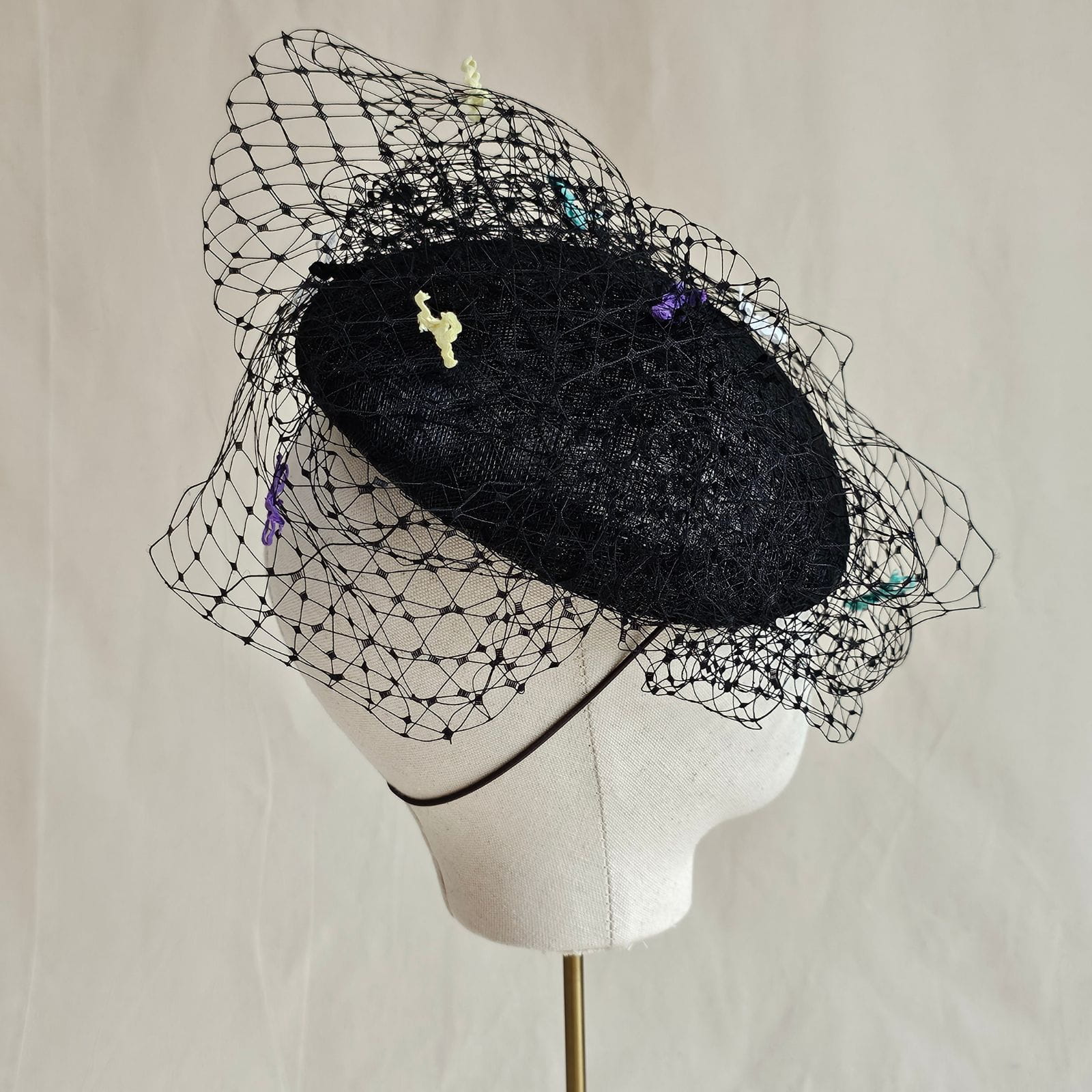 Black sinamay beret with beautiful veil and multicolour bow detailing, side view.