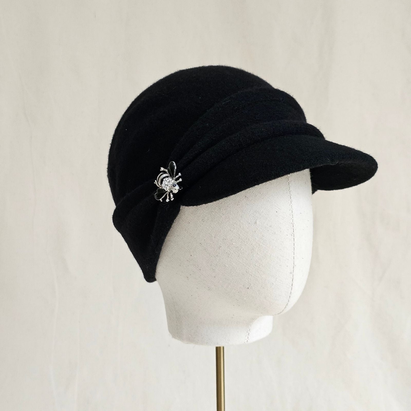 Black wool peak cap with beautiful bee brooch, angle view.