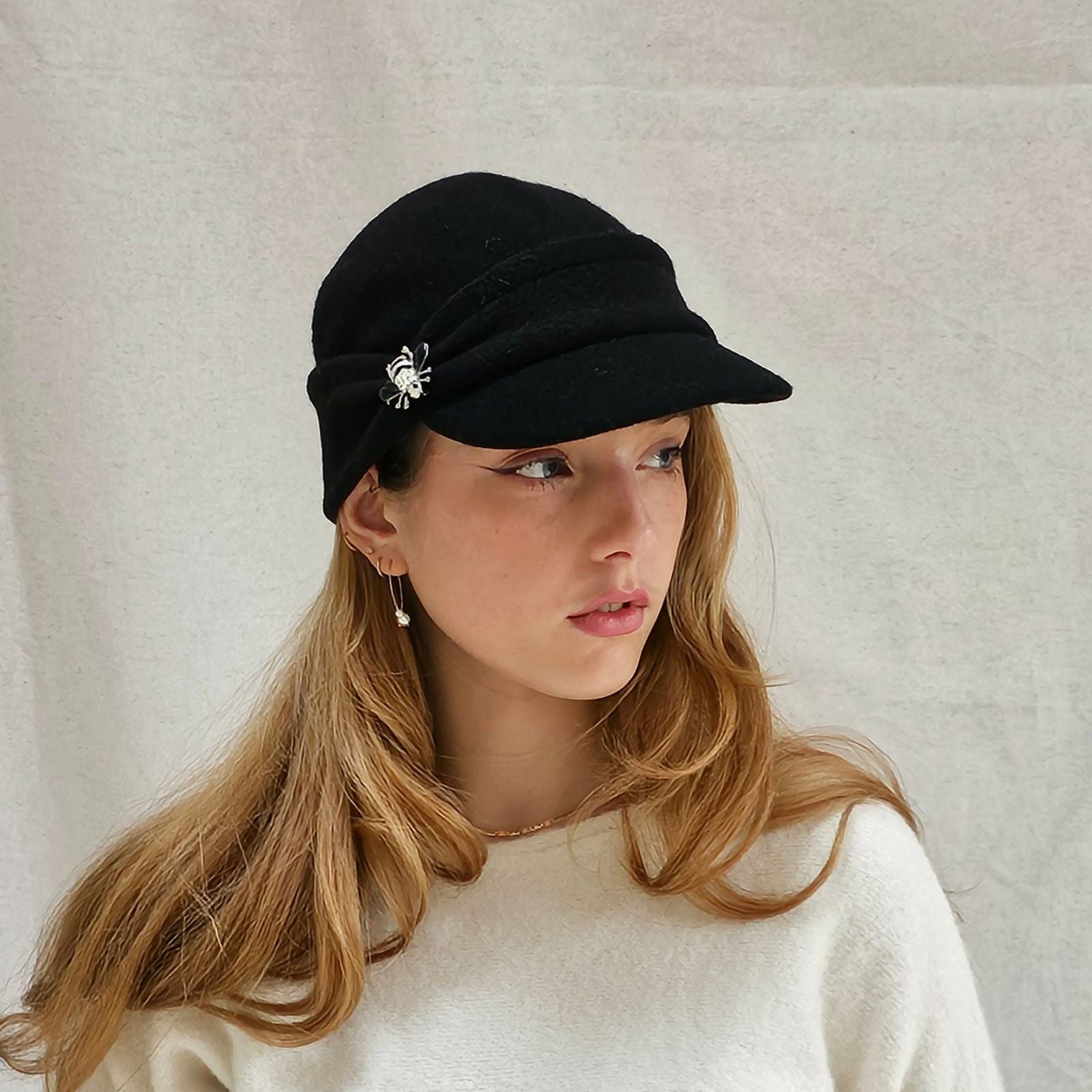 Black wool peak cap with beautiful bee brooch, angle view.