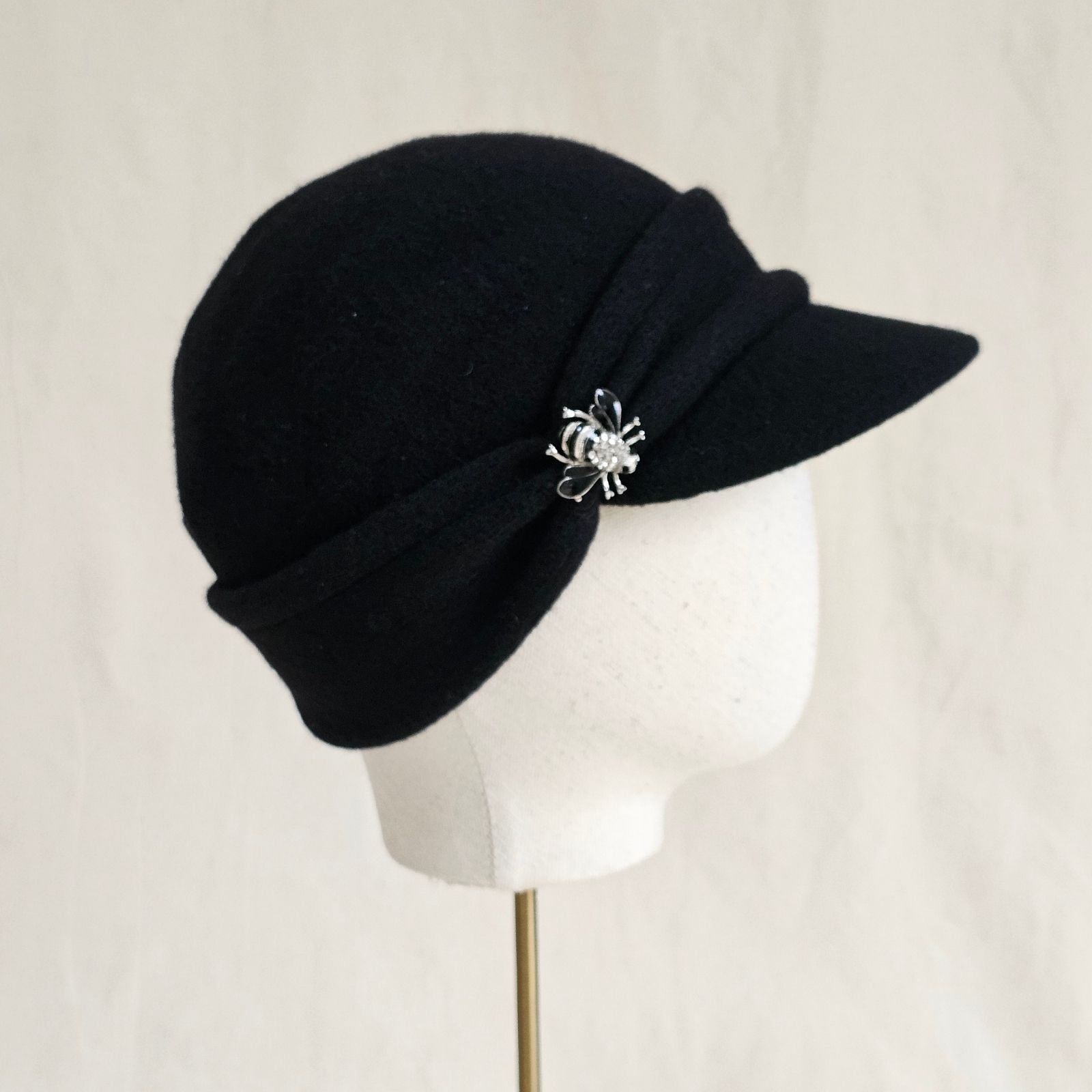 Black wool peak cap with beautiful bee brooch, side view.