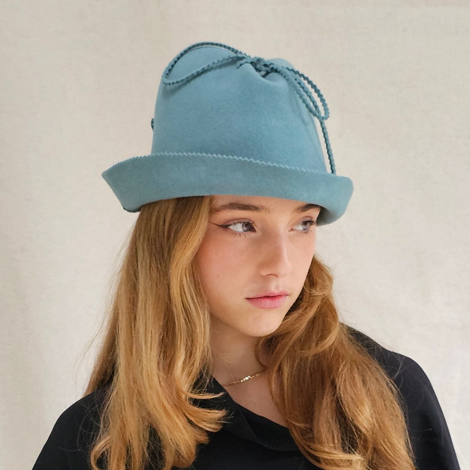 Blue felt trilby with zigzag cut brim and bow embellishment, side view.
