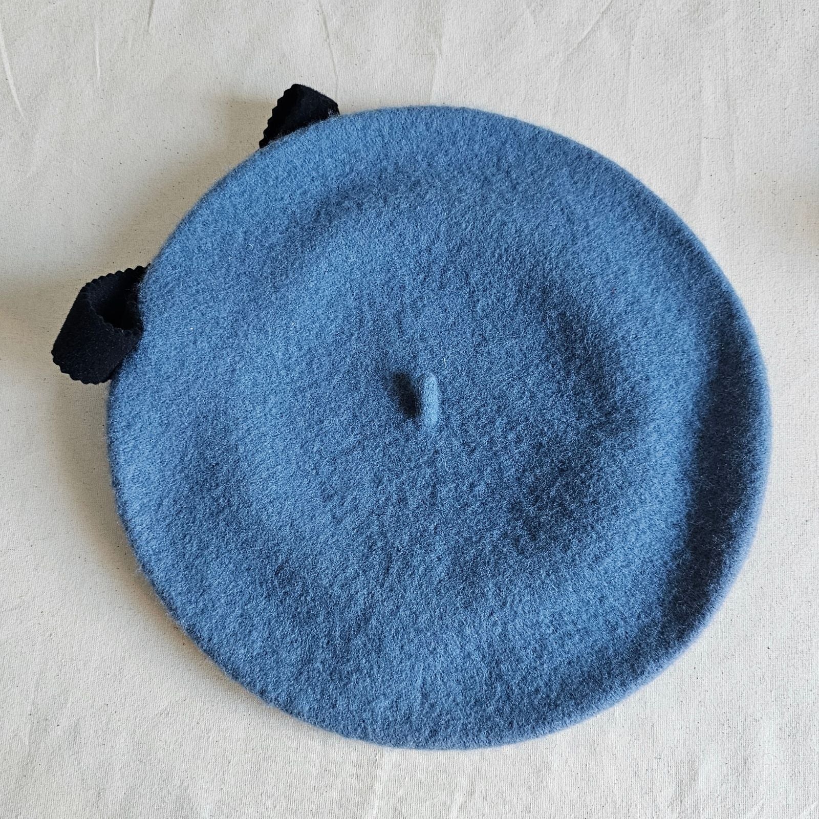 Blue wool beret with black bow embellishment, top view.