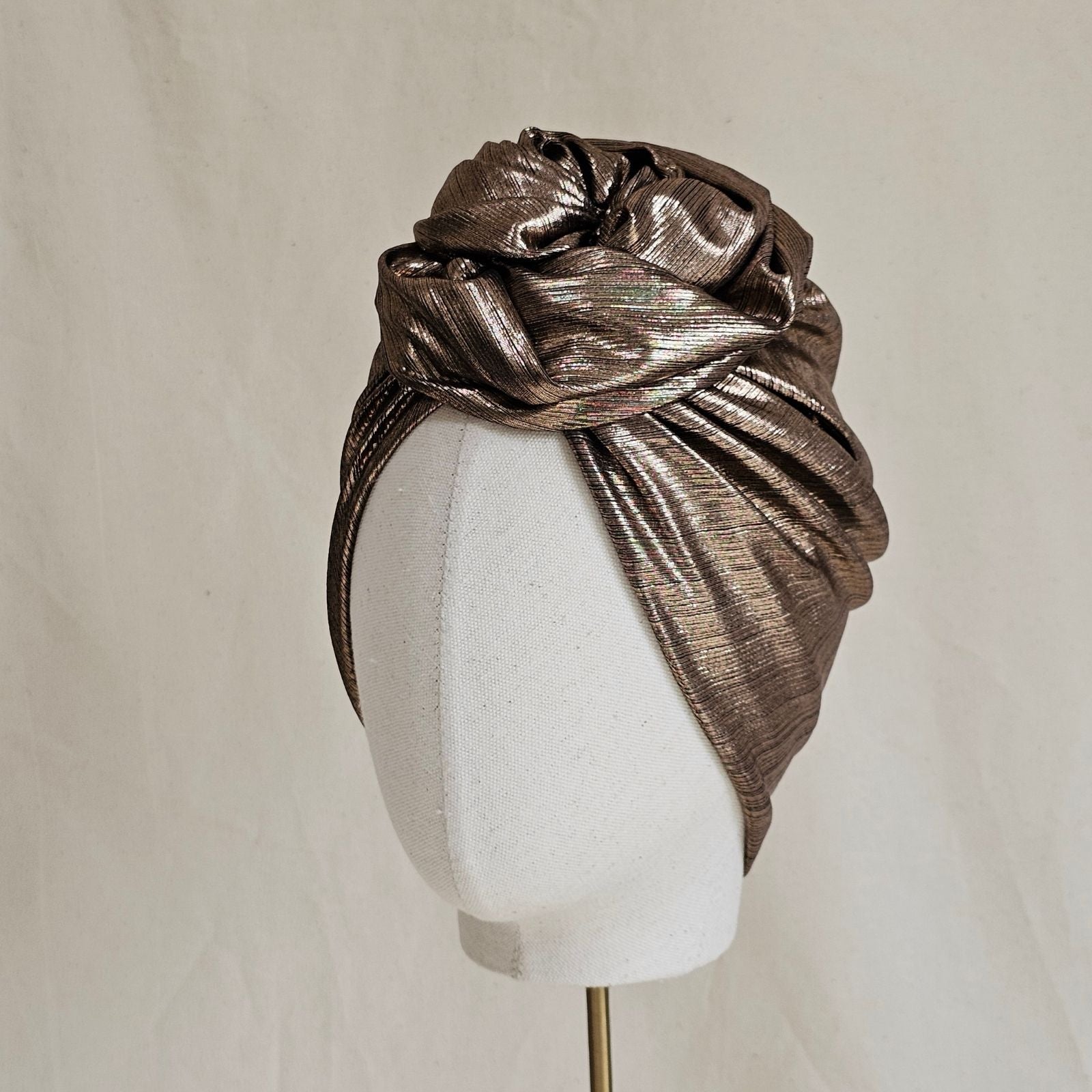 Copper lamé softly gathered turban with sculptural rose knot, angle view.