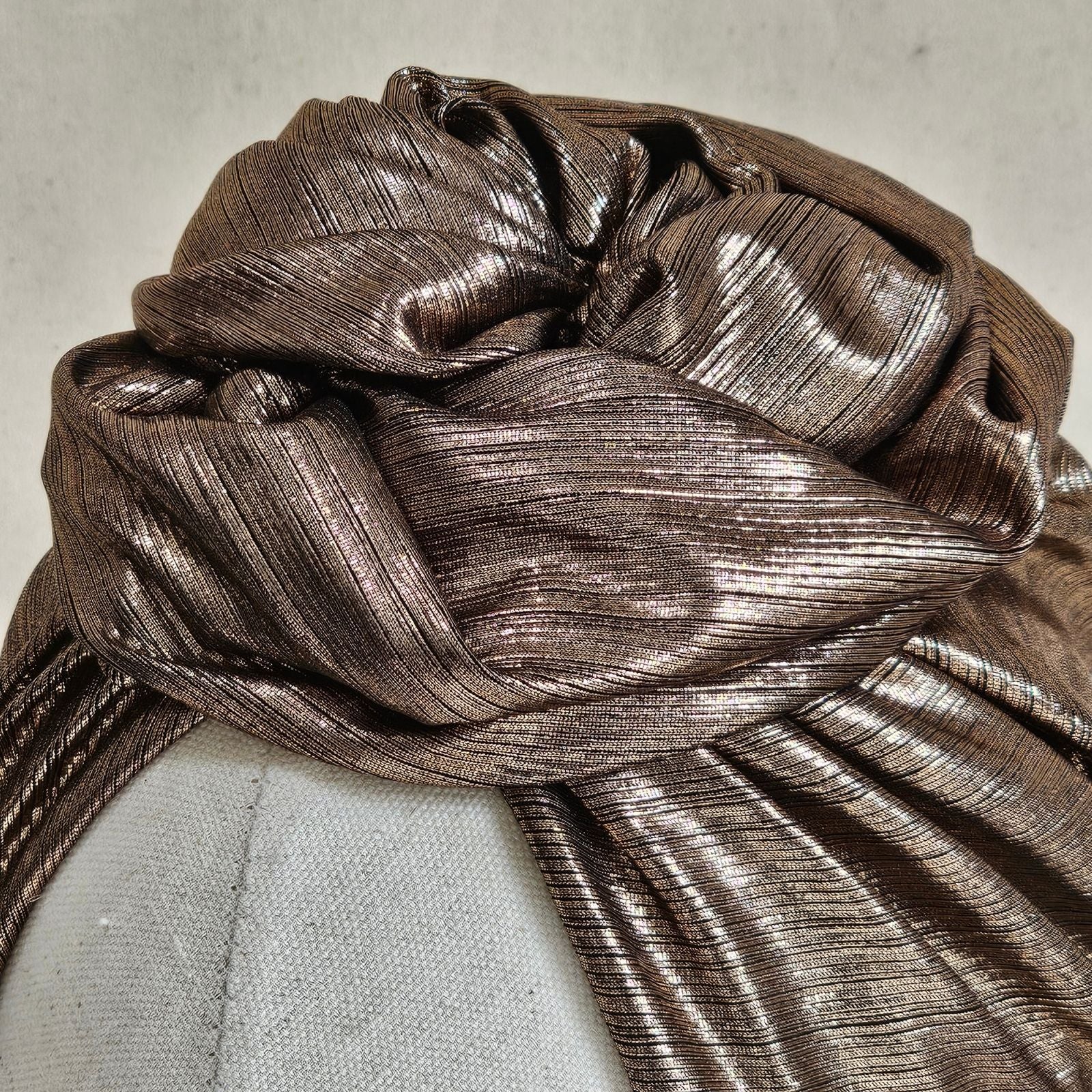 Detail of copper lamé turban with sculptural rose knot.