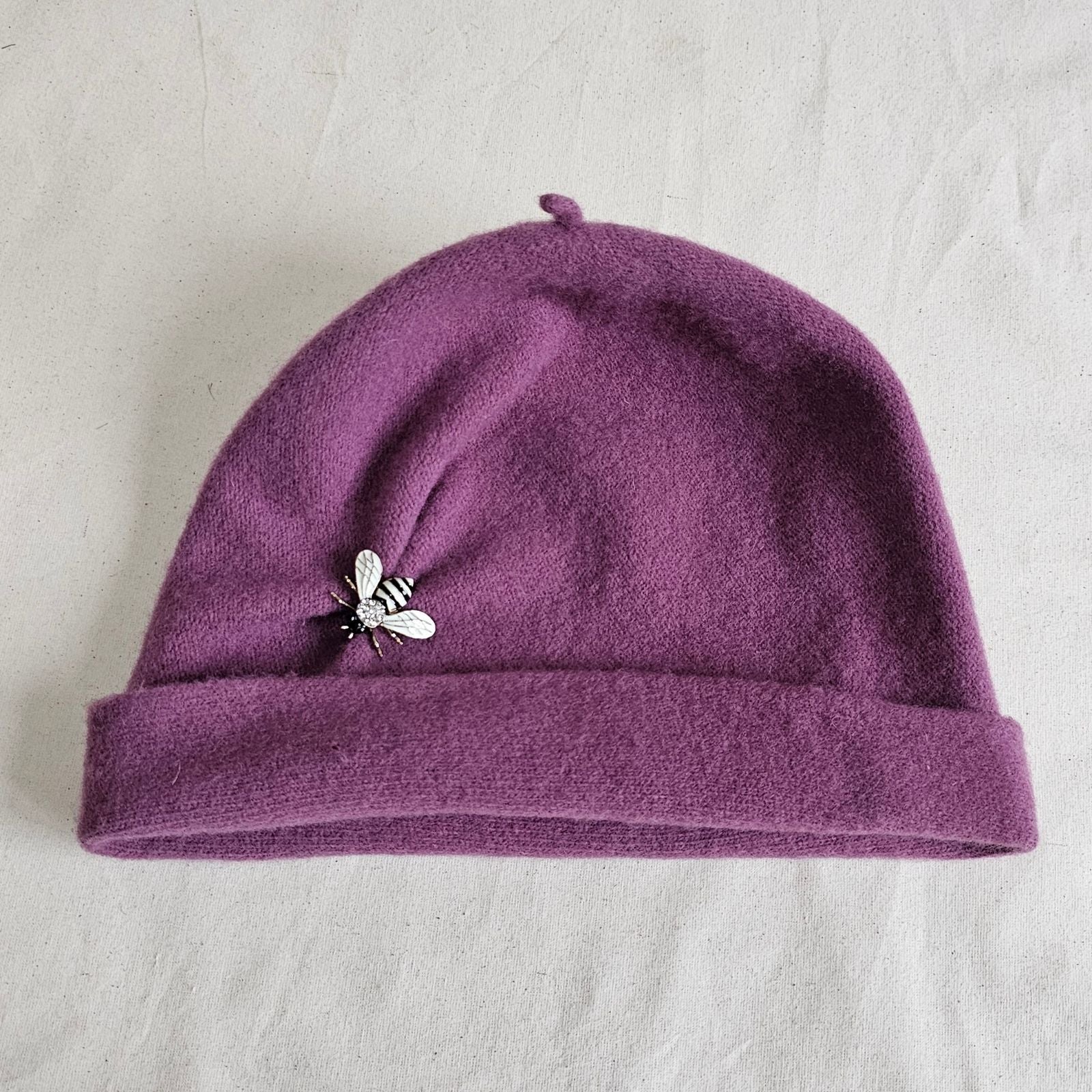 Dusky pink wool beanie with beautiful bee brooch, top view.