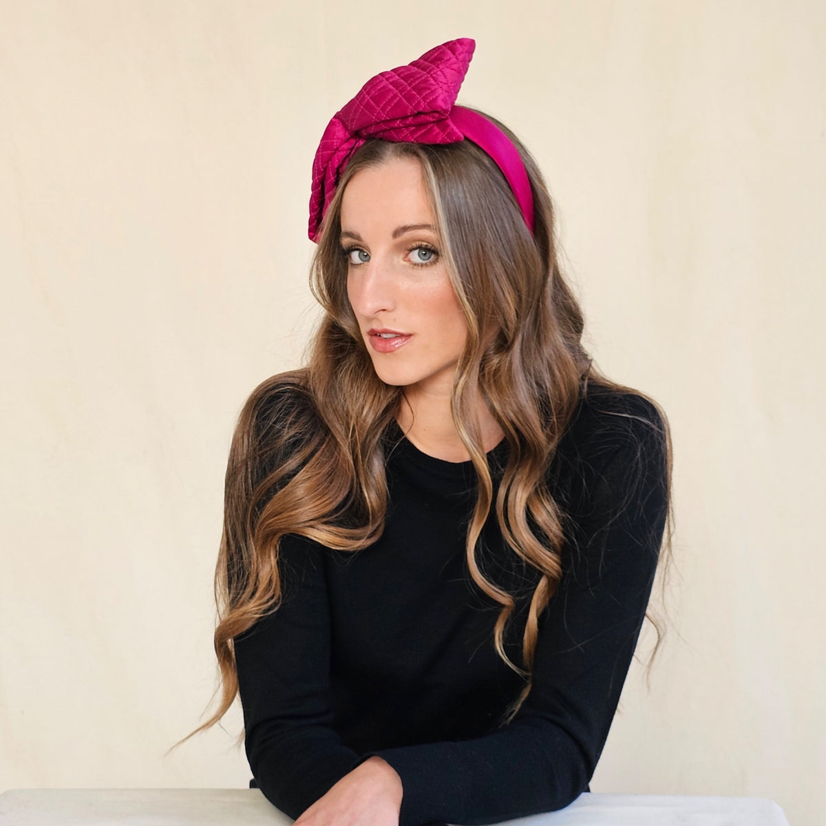 Angled view of fuchsia quilted silk bow headband on a seated
model.