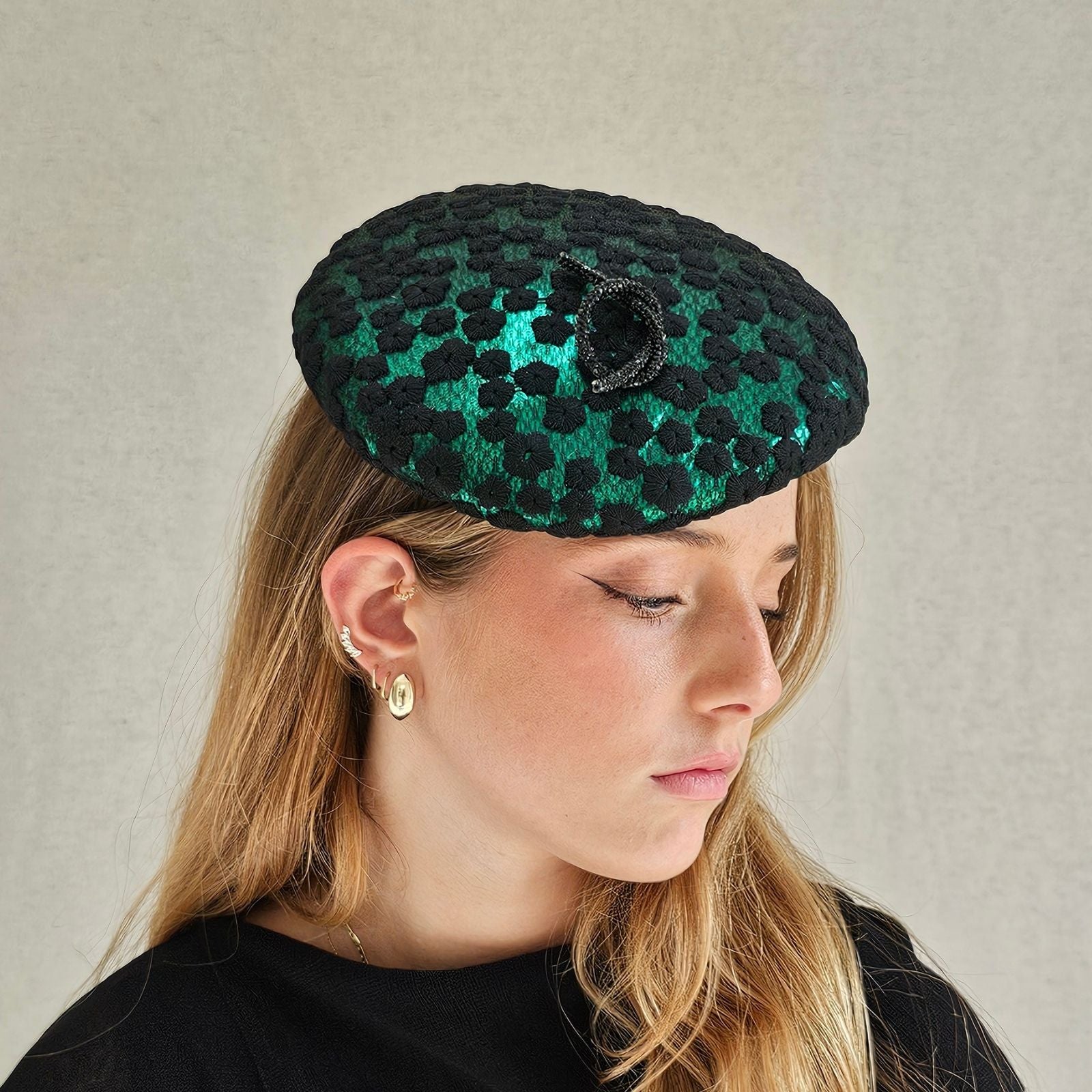 Green beret covered with black flower lace and beautiful black pretzel knot embellishment, angle view.