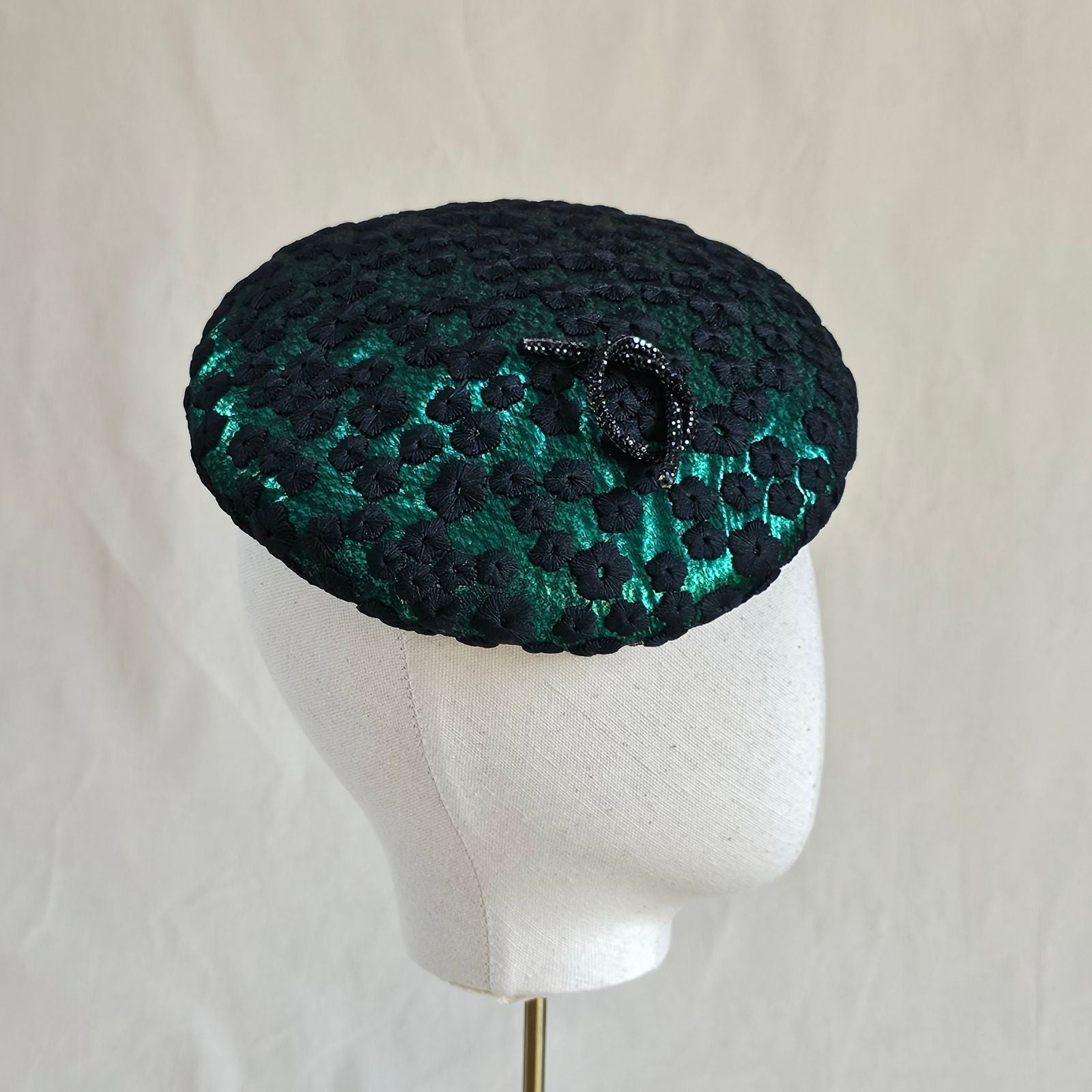 Emerald green beret with black flower lace and elegant brooch embellishment, right view.