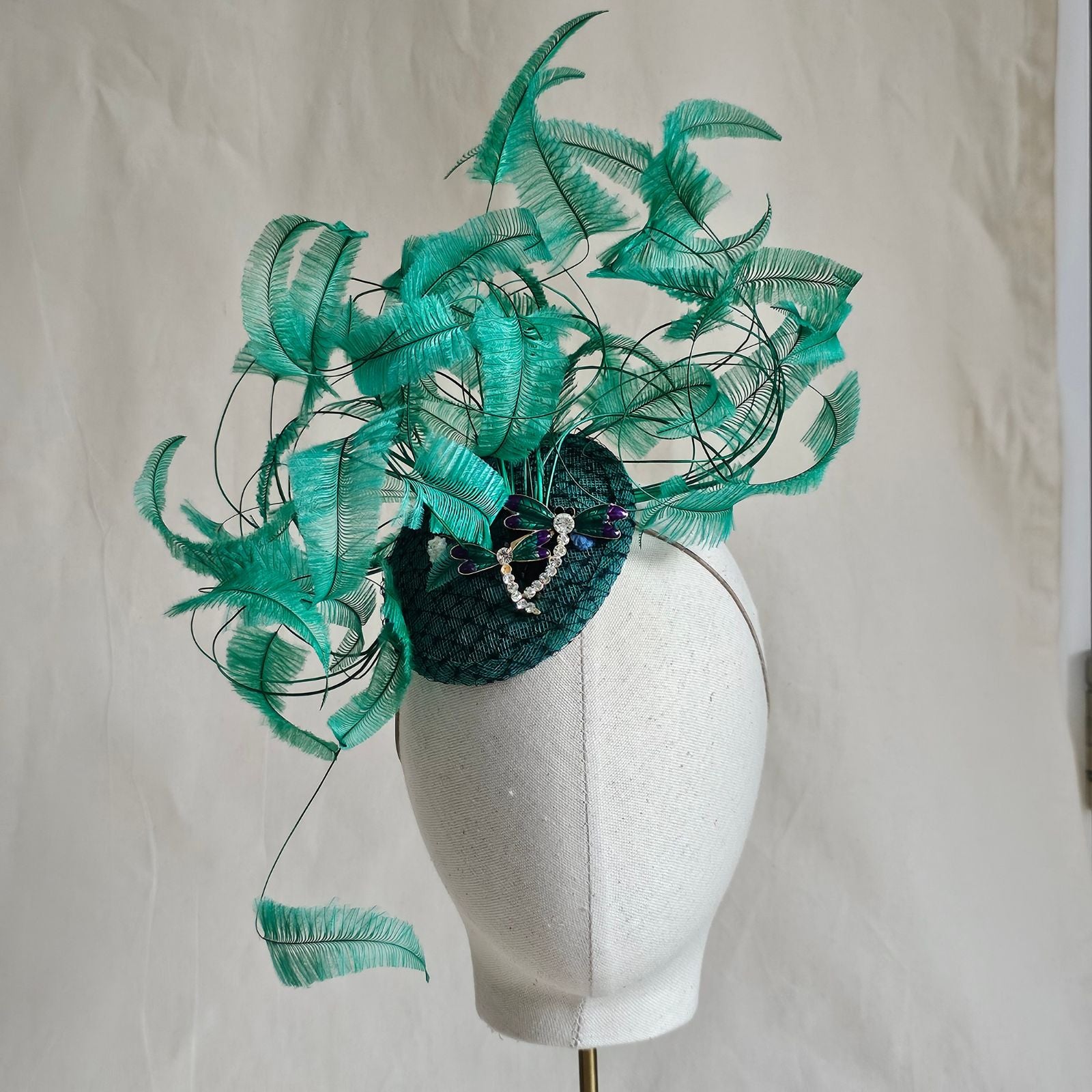 Green fascinator with elegant curled feathers and beautiful dragonfly embellishments, front view.