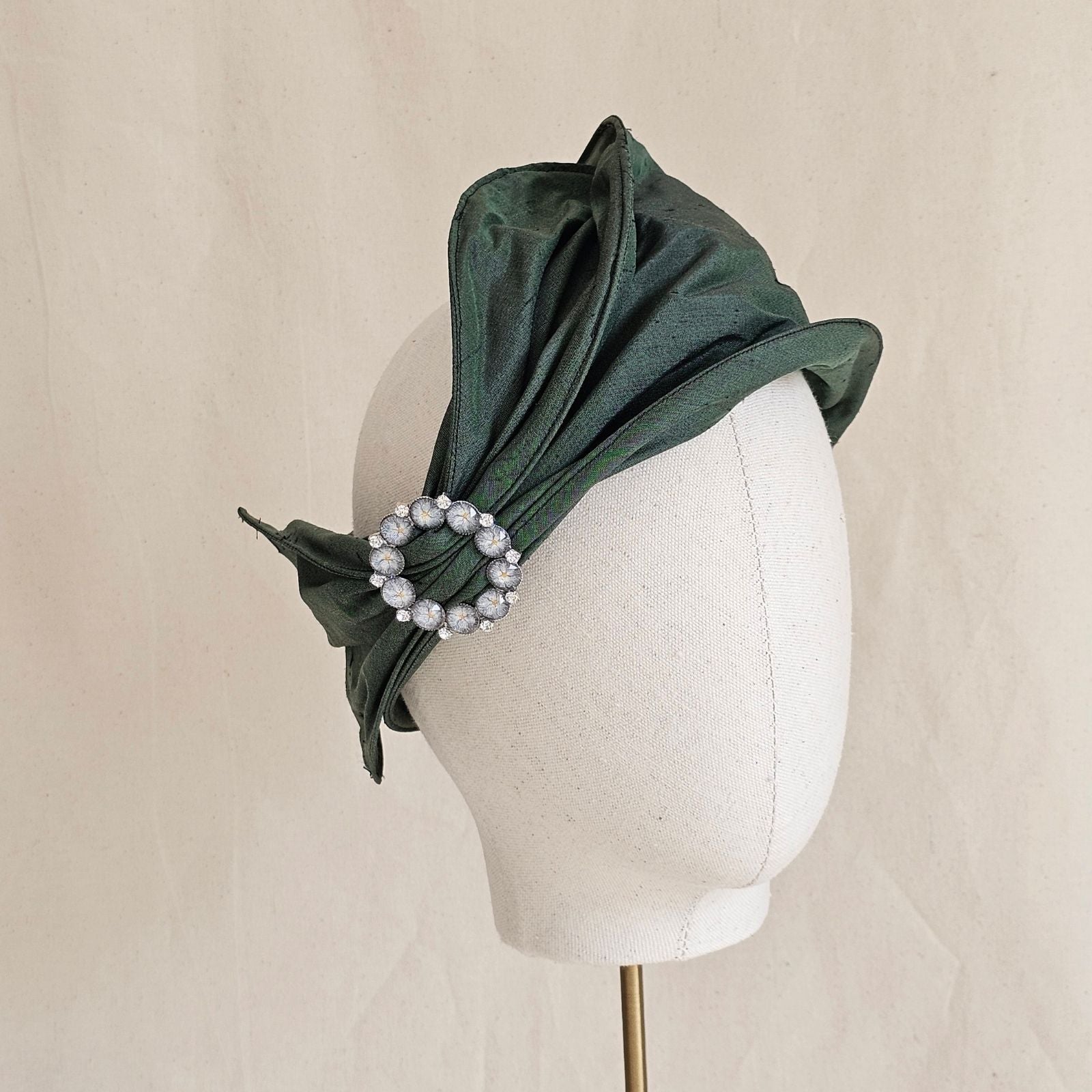 Green silk head wrap with decorative brooch, angle view.