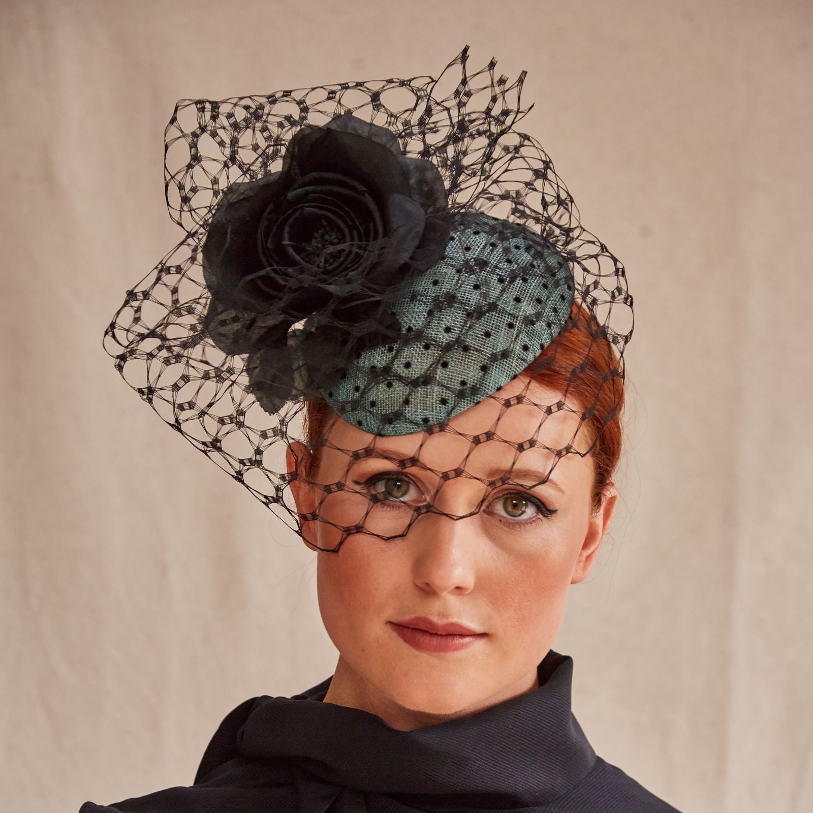 Green sinamay beret with intricate black veiling and flower embellishment, front view.