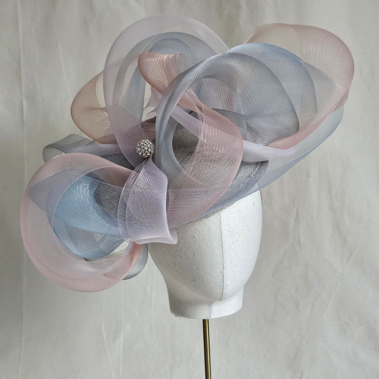 Grey, blue and pink crin swirl ascot hat with crystal diamanté globe embellishment, front view.