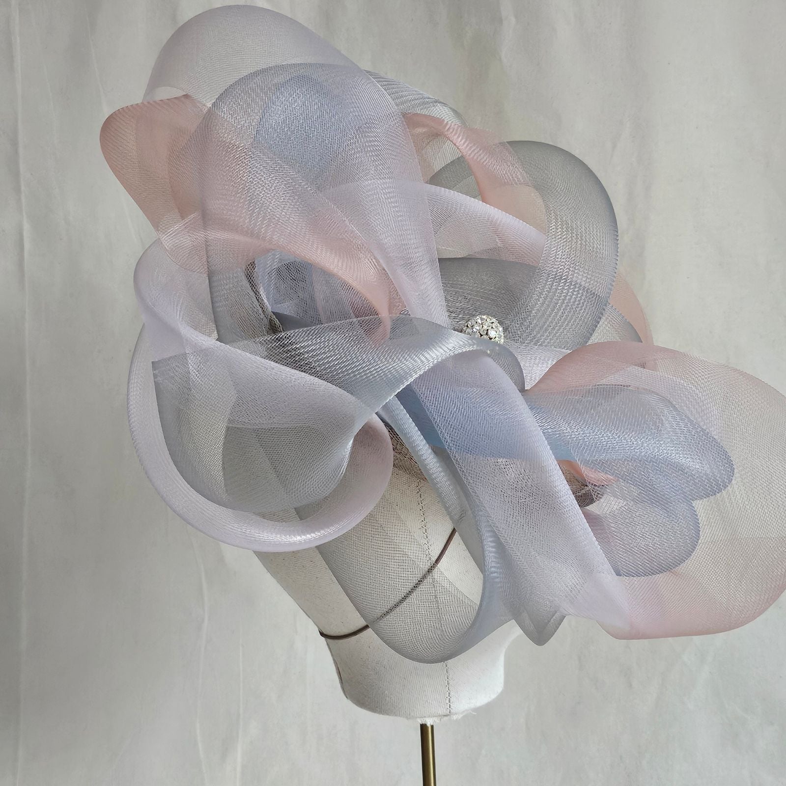 Grey, blue and pink crin swirl ascot hat with crystal diamanté globe embellishment, angle view.