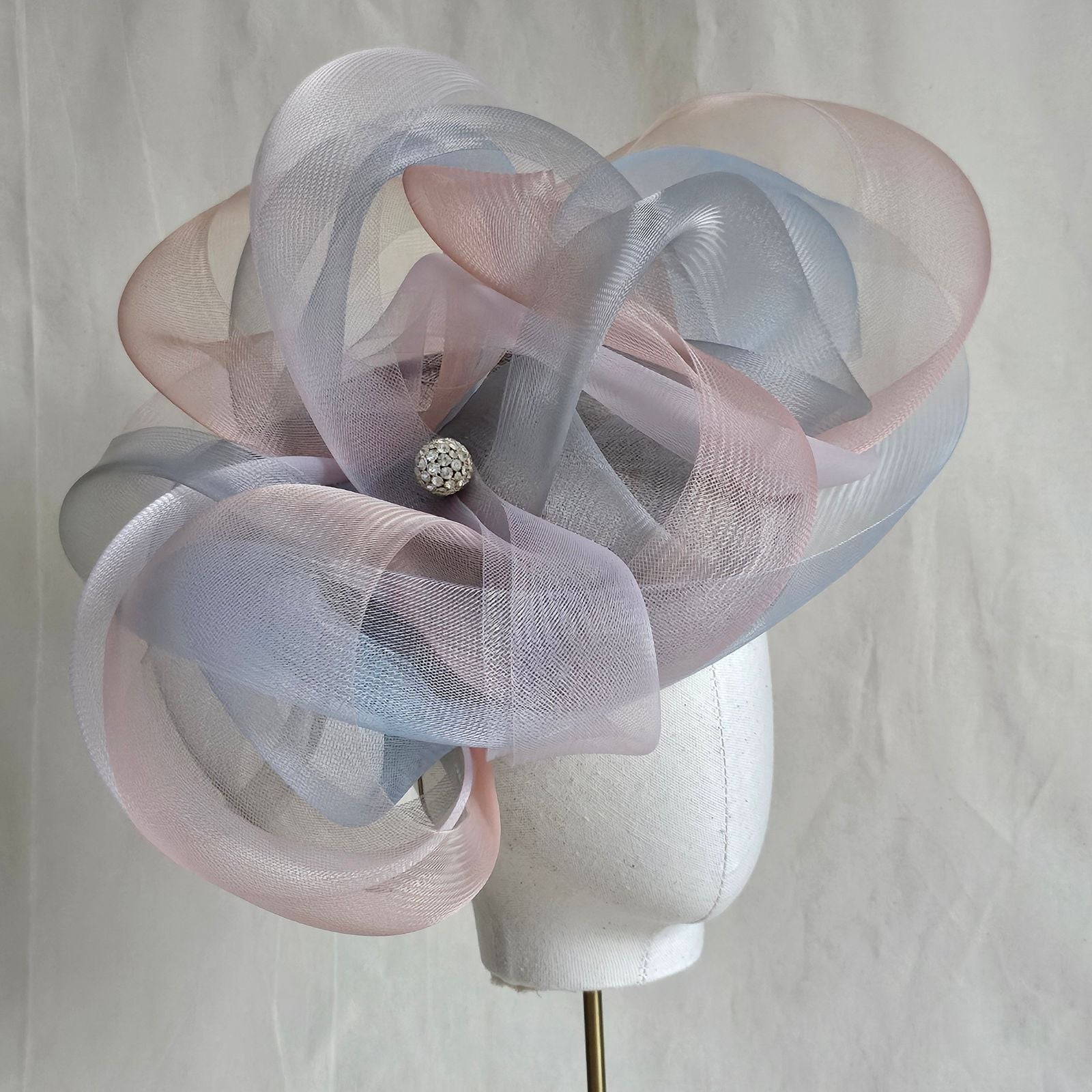 Grey, blue and pink crin swirl ascot hat with crystal diamanté globe embellishment, side angle view.