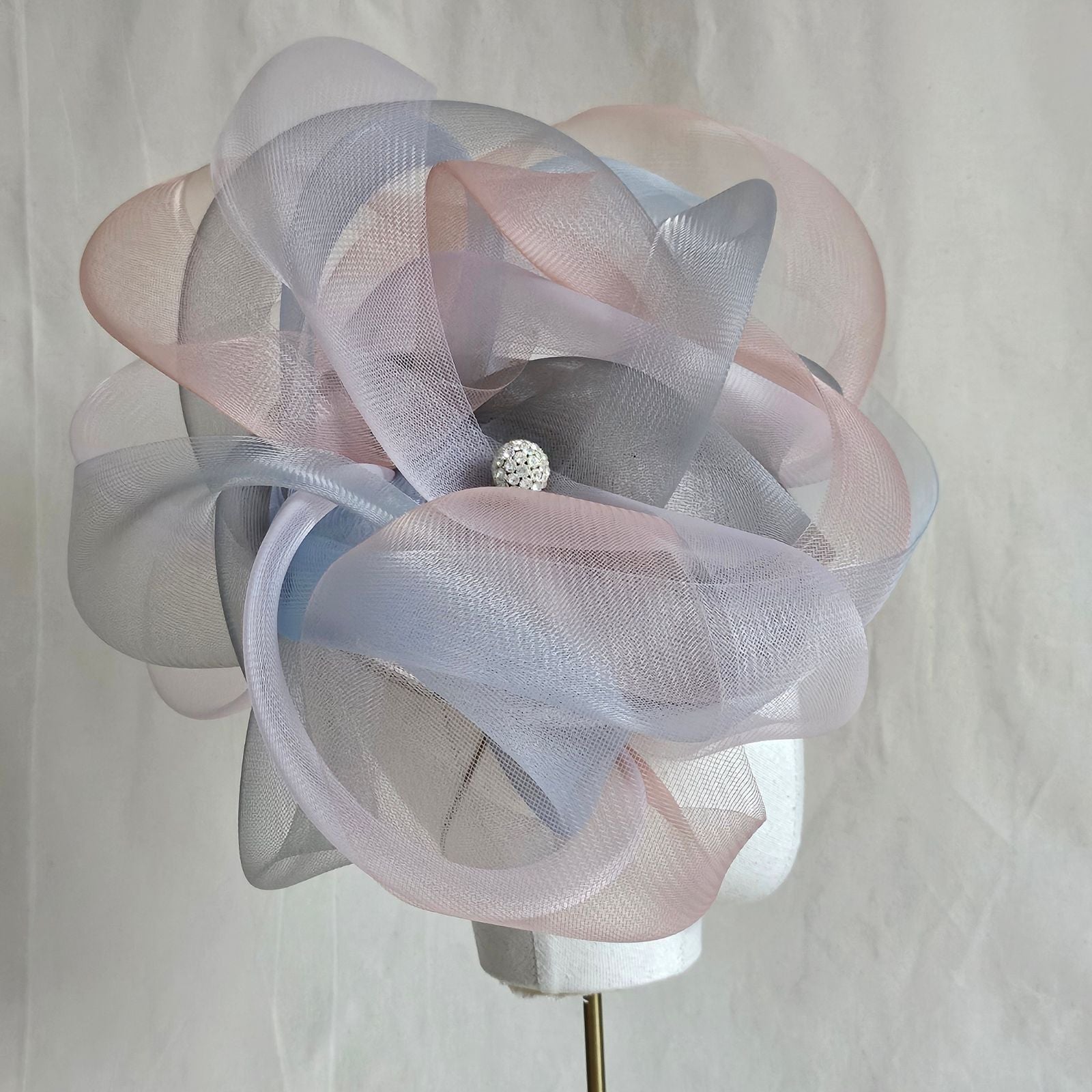 Grey, blue and pink crin swirl ascot hat with crystal diamanté globe embellishment, side view.