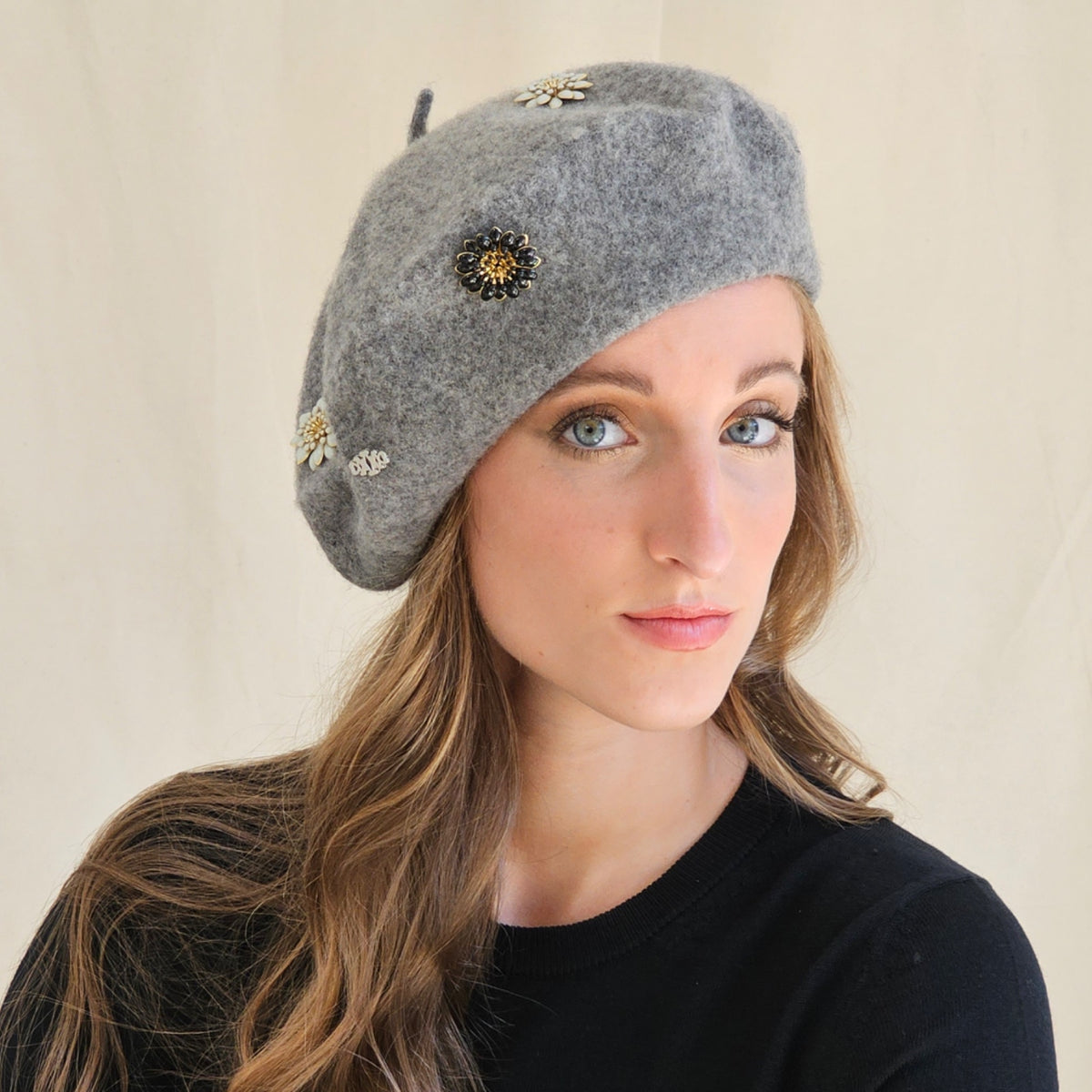 Close-up of grey wool beret showing flower and monogram details.