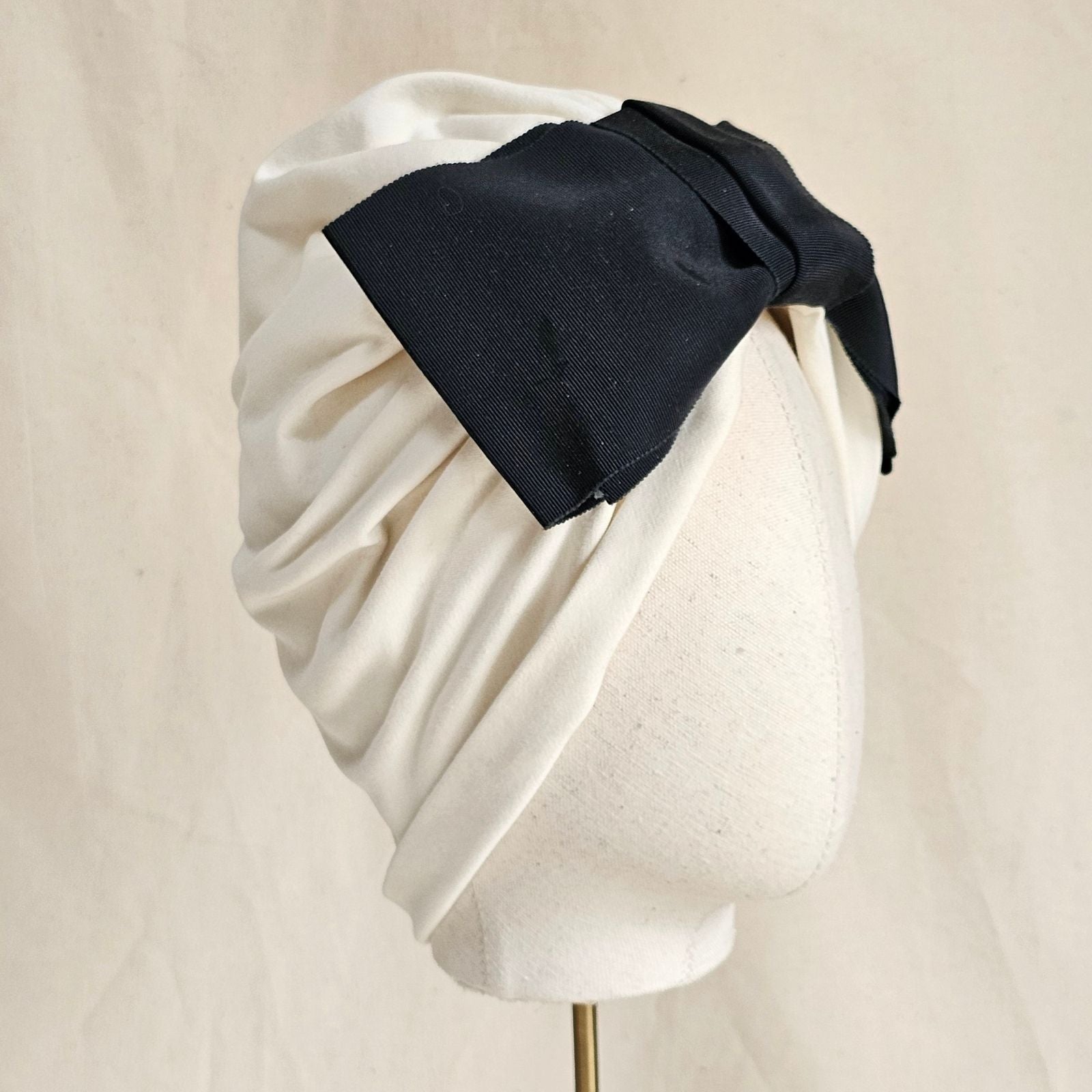 Ivory loosely gathered turban with dramatic black petersham bow, side view.