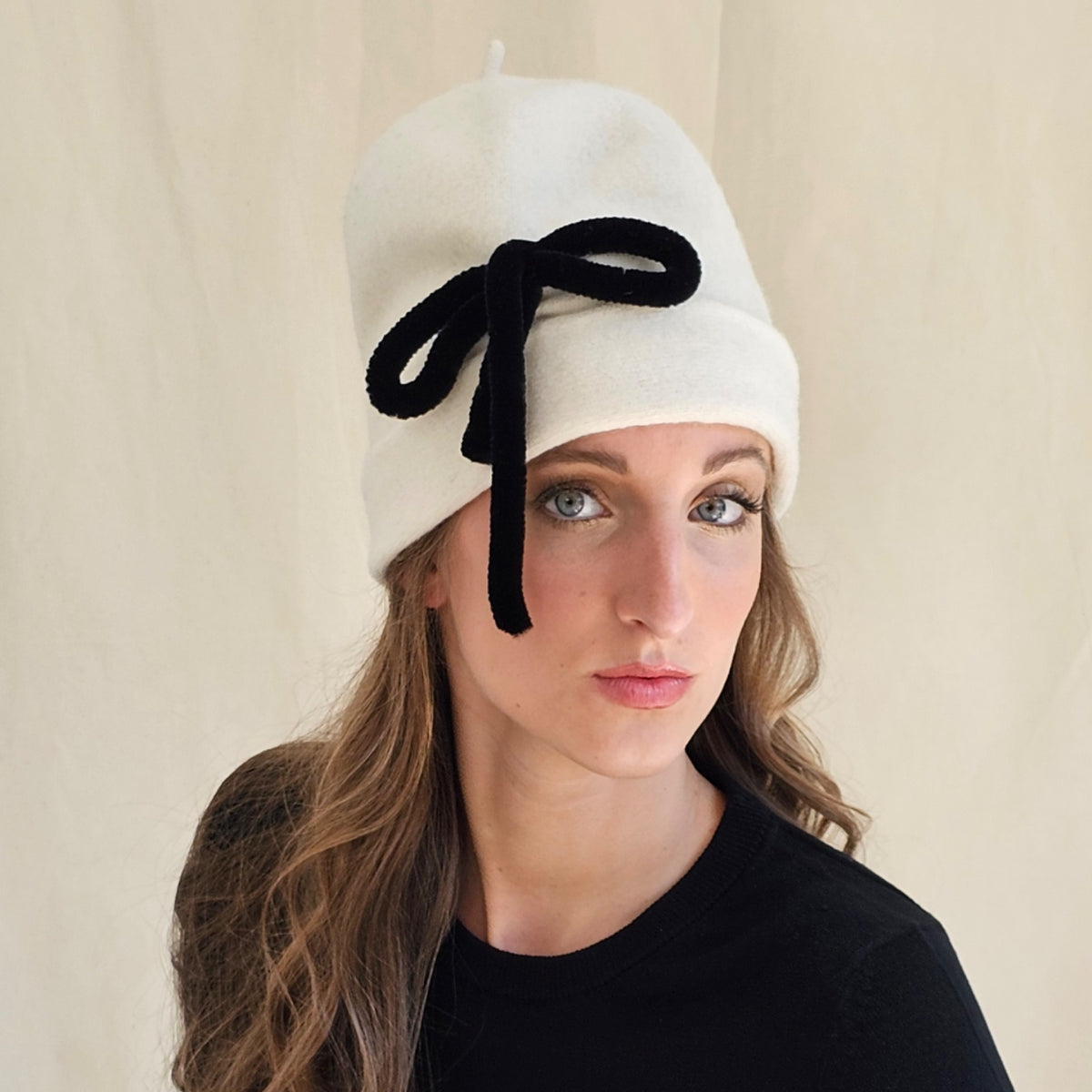 Close-up of ivory wool beanie showing black bow and trailing ends.