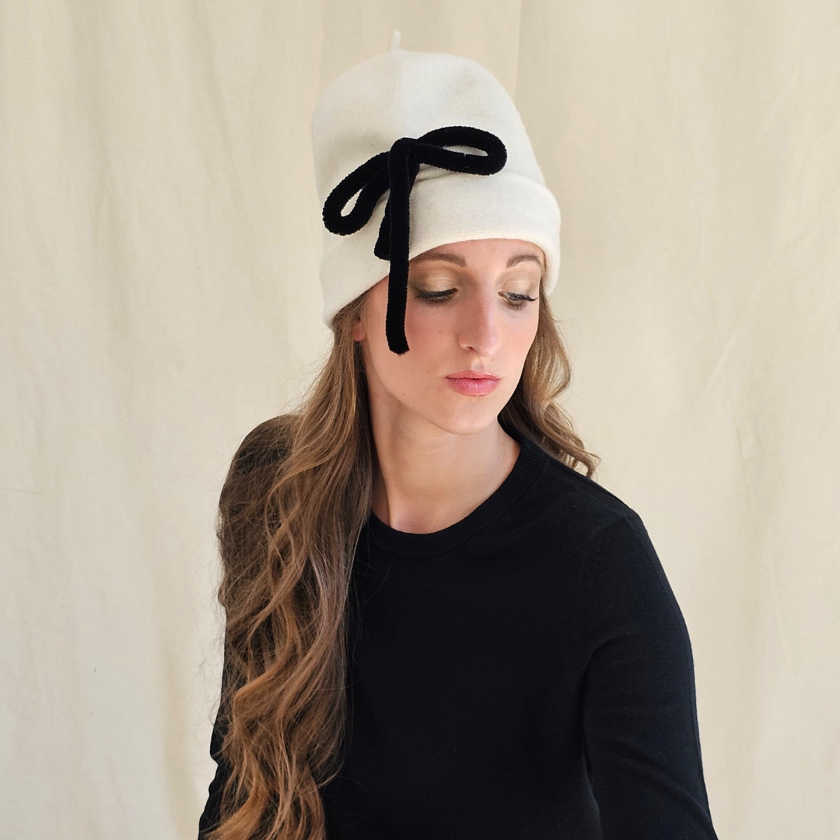 Ivory gathered wool beanie with a black bow, worn on a model.