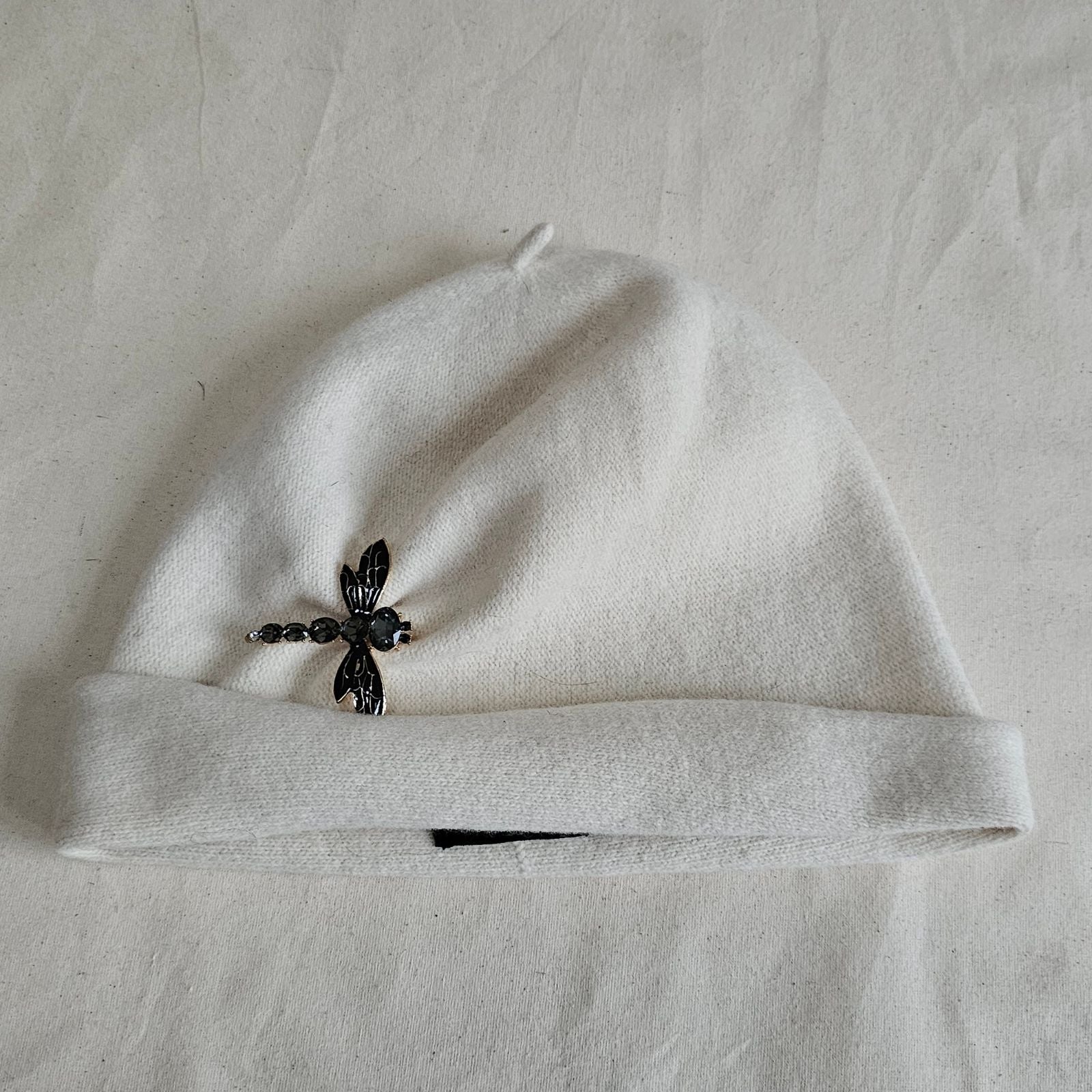 Ivory wool beanie with beautiful dragonfly brooch, top view.