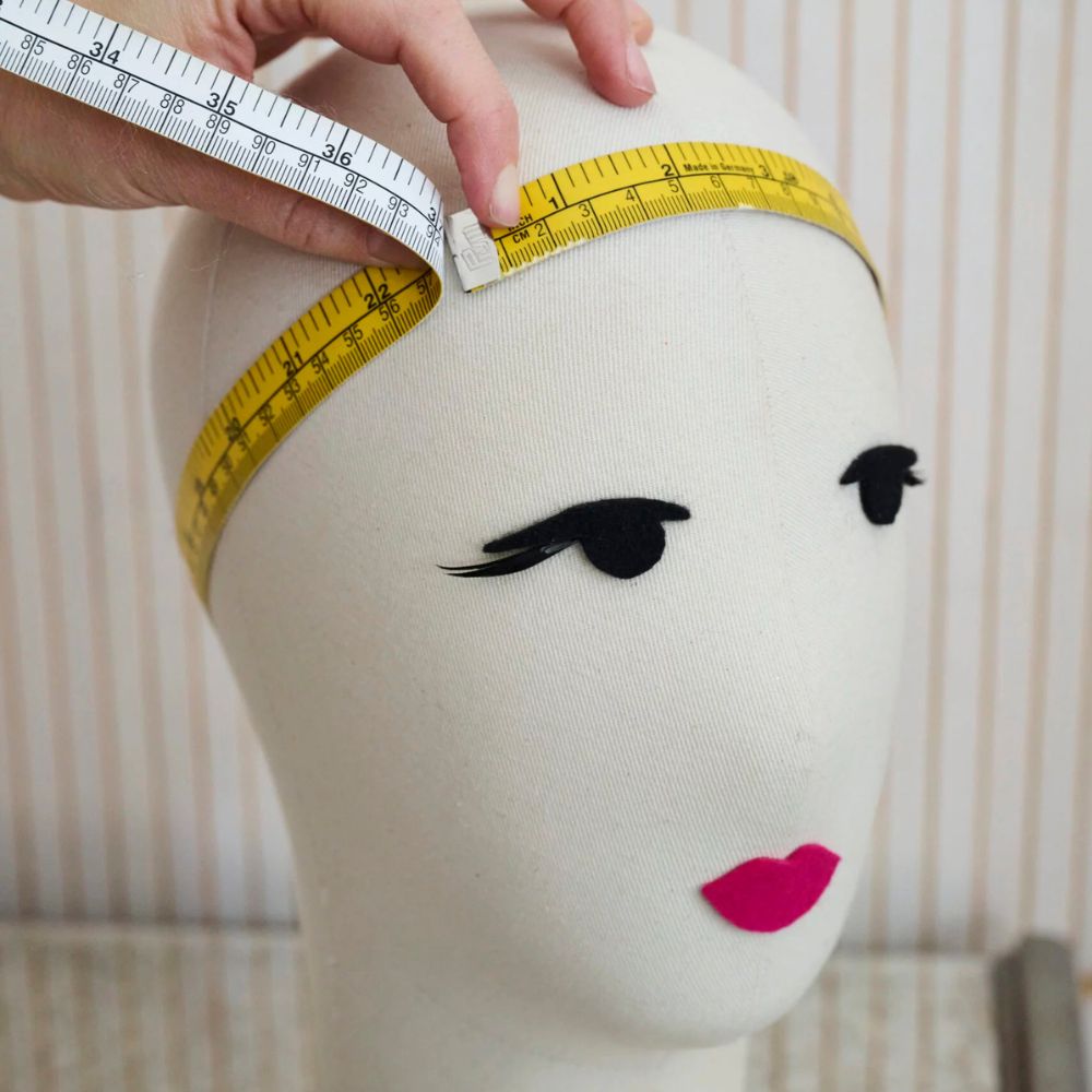 Mannequin head with face makeup and measuring tape, used for fashion or design purposes.