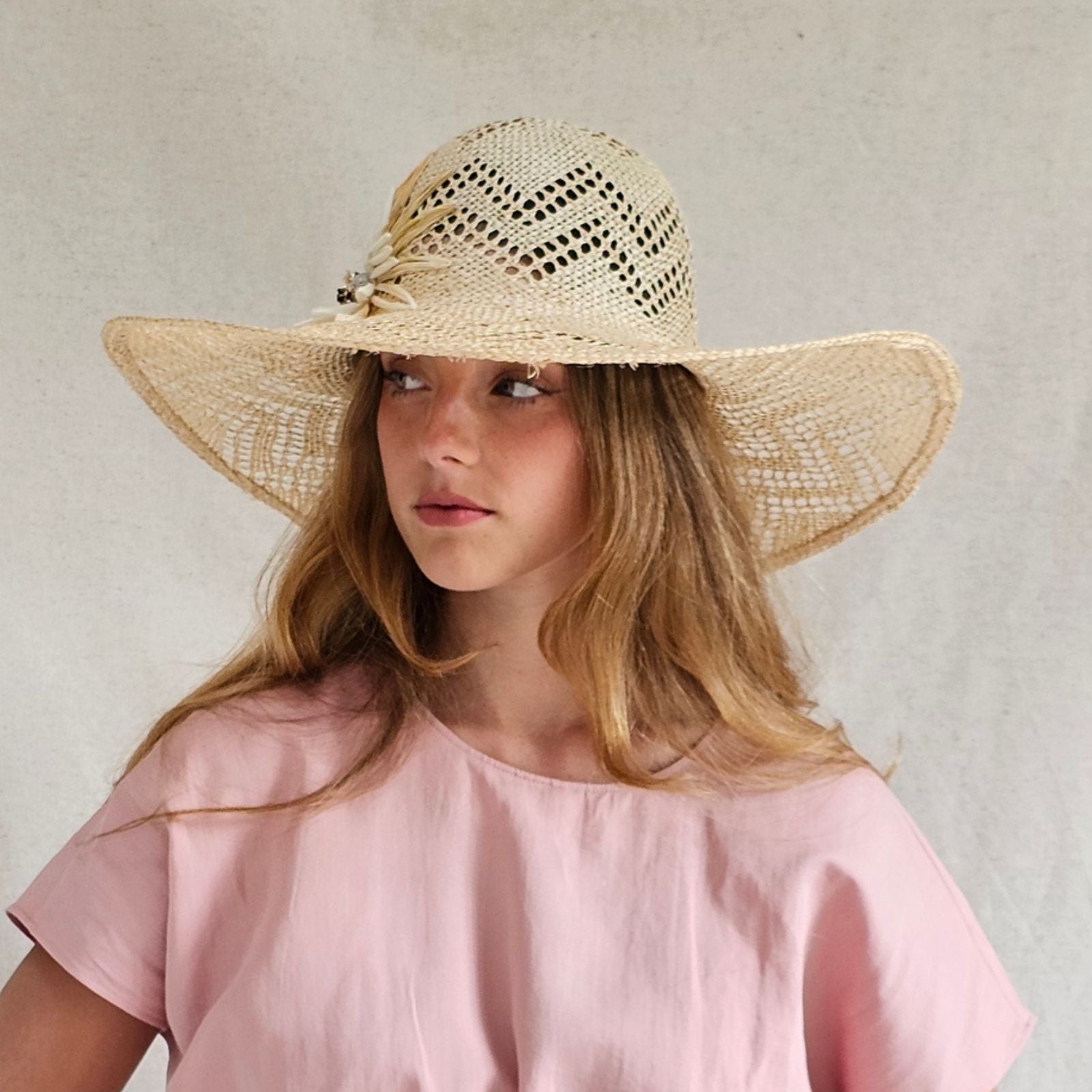 Natural mesh straw sunhat with beautiful flower embellishment, angle view.