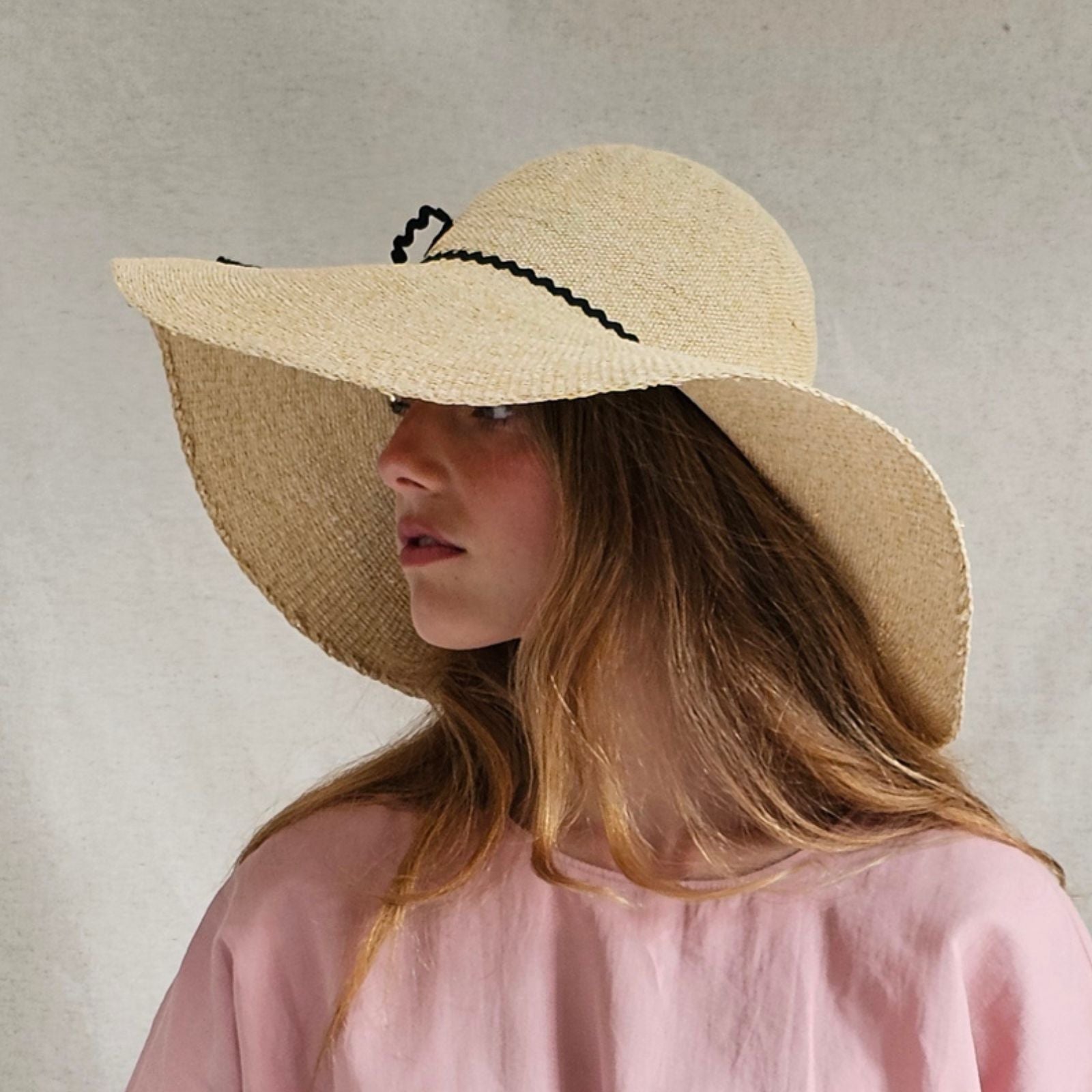 Natural straw sunhat with elegant black bow embellishment, side view.