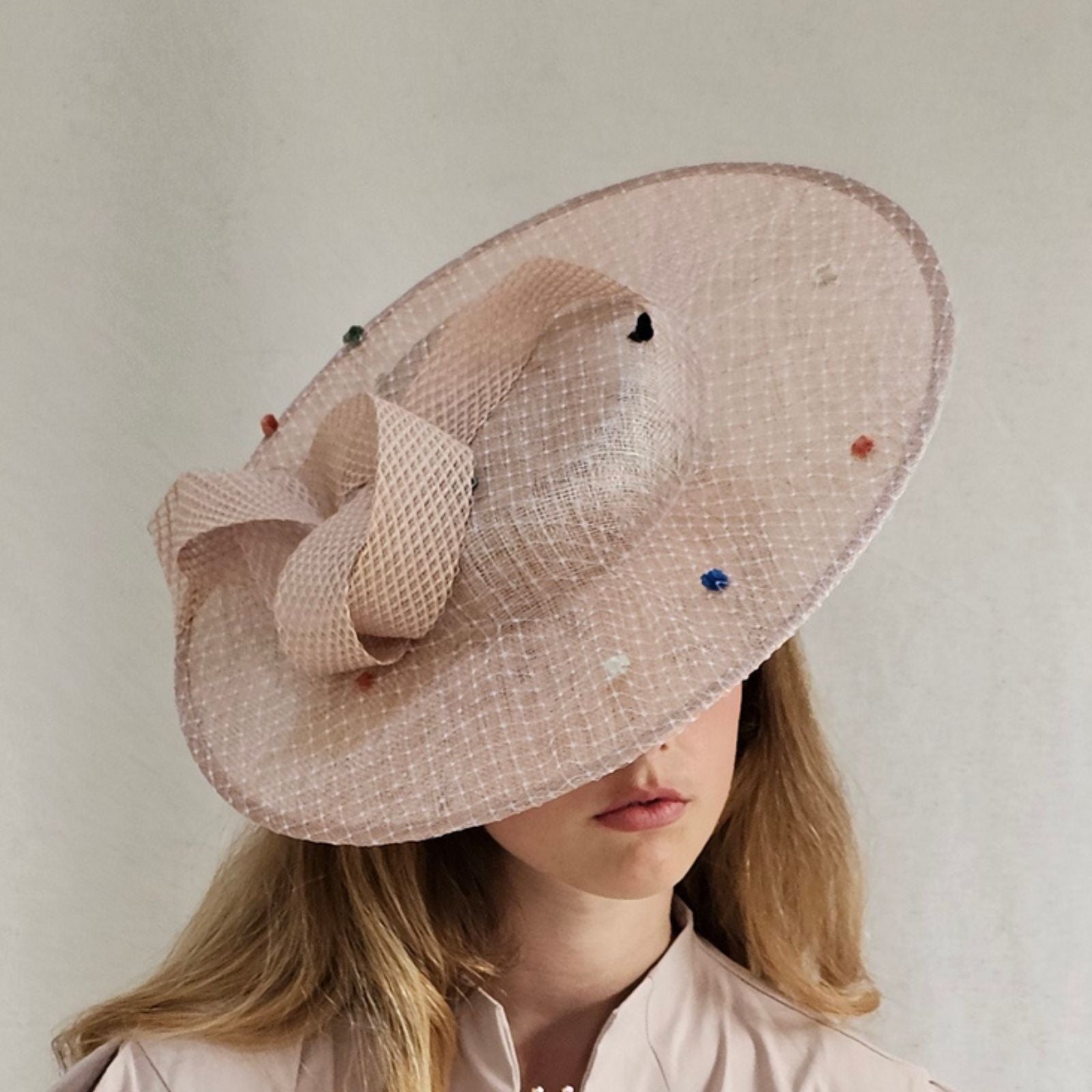Nude sinamay boater hat with dot veiling and elegant swirl embellishment, angle view.