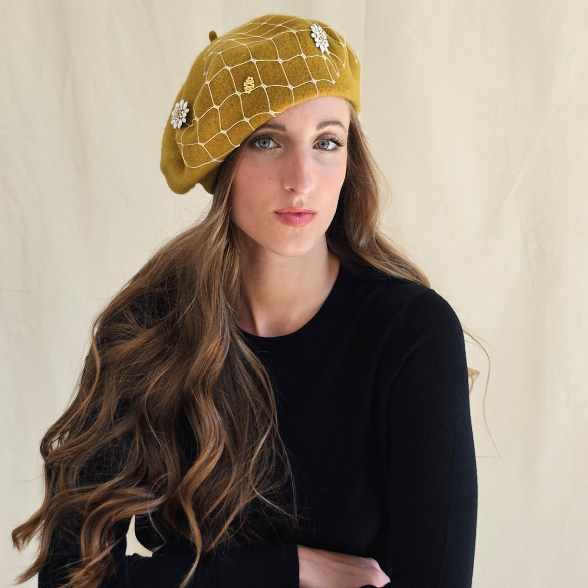 Angled view of ochre wool beret with white flowers, gold
monograms and ivory veiling.