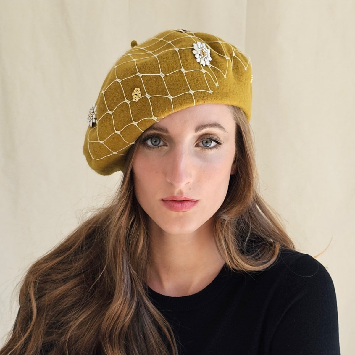 Ochre wool beret with white flowers and ivory veiling, worn on a
model.