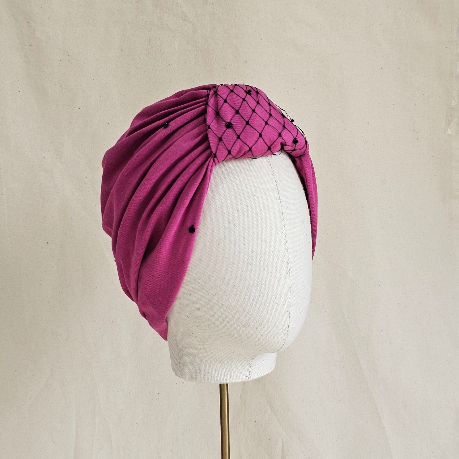 Pink jersey turban with decorative black veiling over central loop and tiny blqck sequin details, angle view.