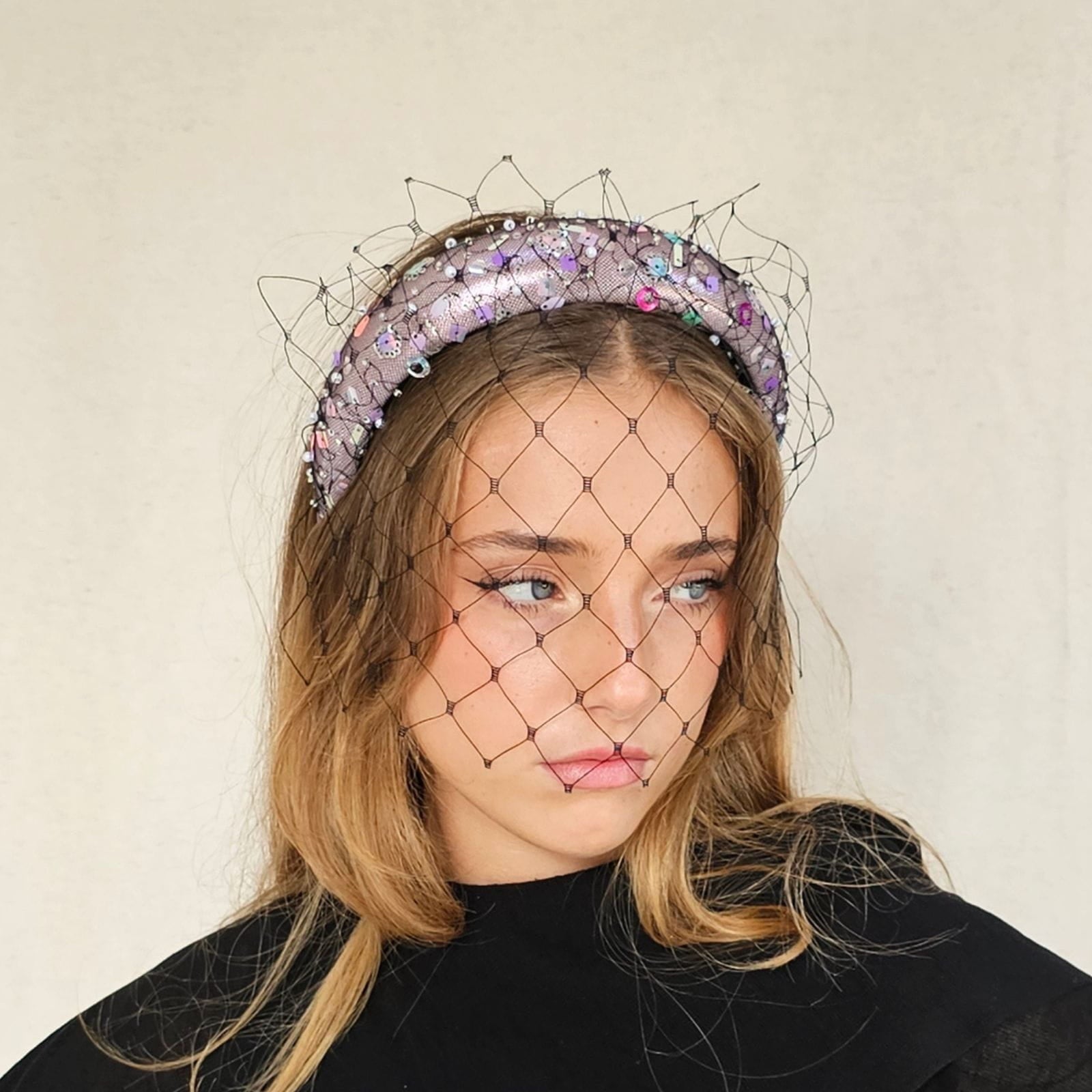 Pink lamé headband with multicolour sequins and black mesh veil, side view.