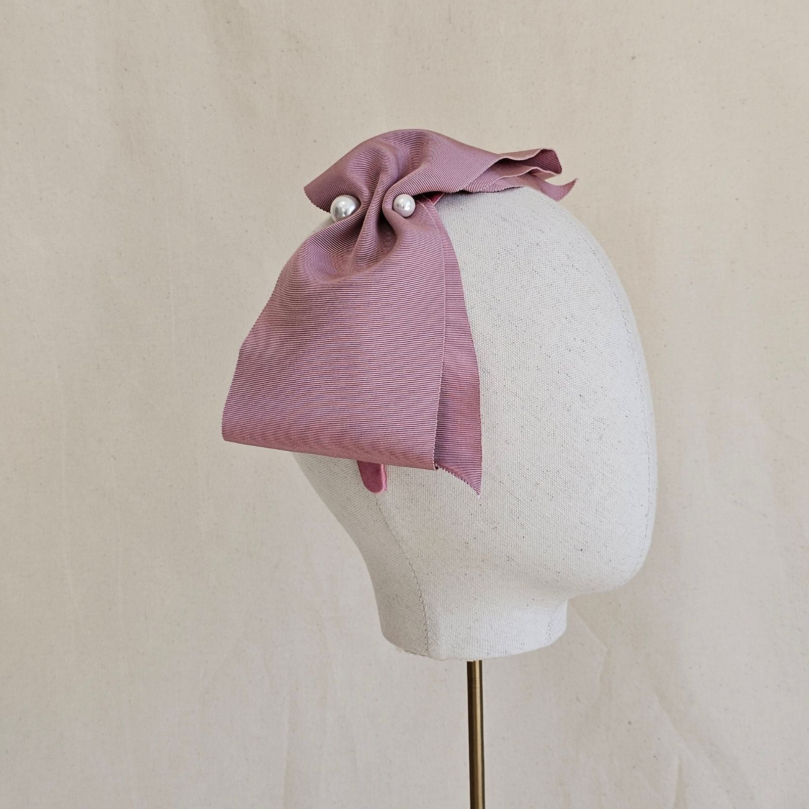 Pink wide petersham bow with 2 central pearls, on a headband, side view.