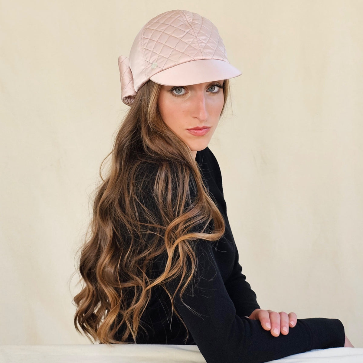 Blush pink quilted silk satin baseball cap, worn on a seated model.