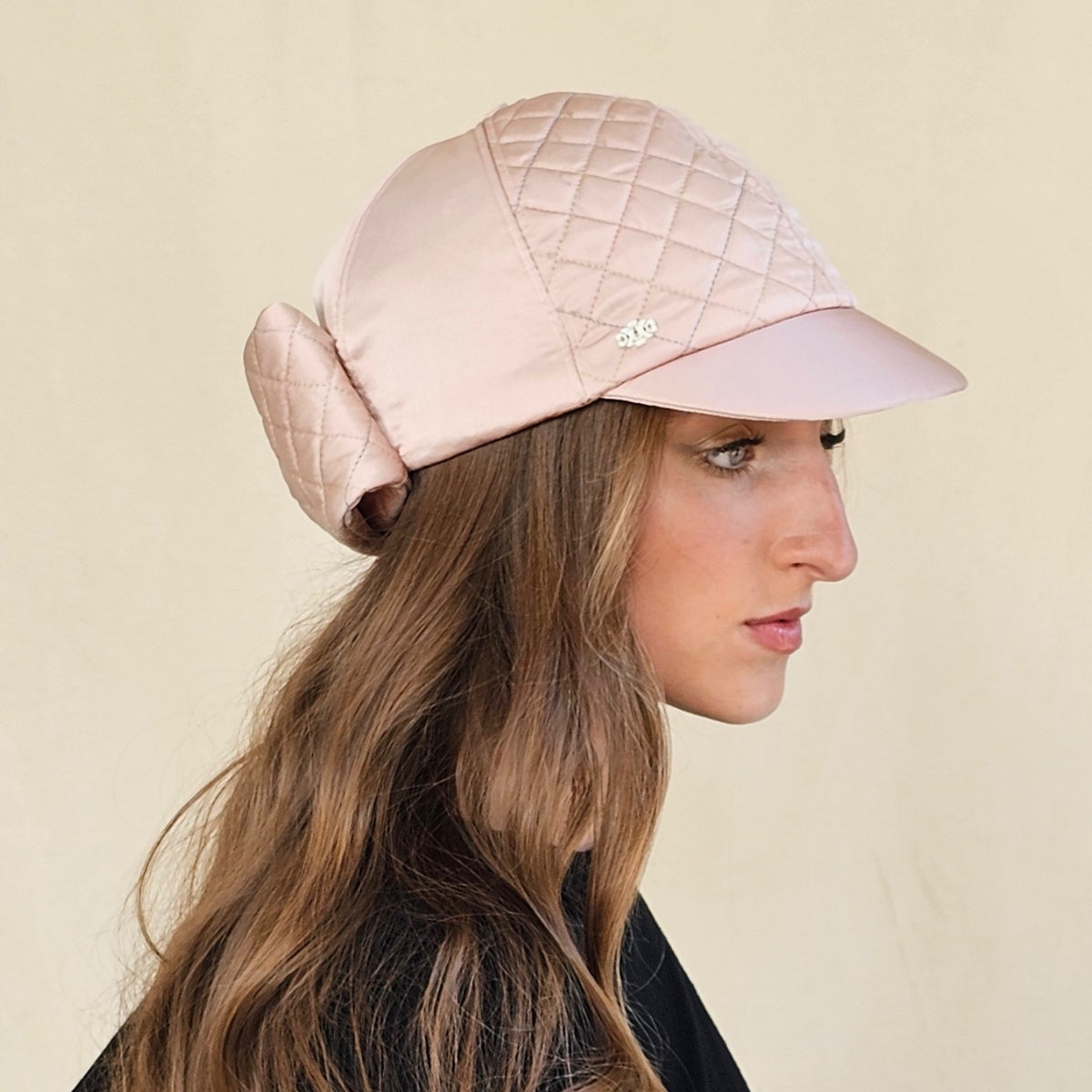 Side view of blush pink silk satin baseball cap showing quilted
panels and back bow on model.