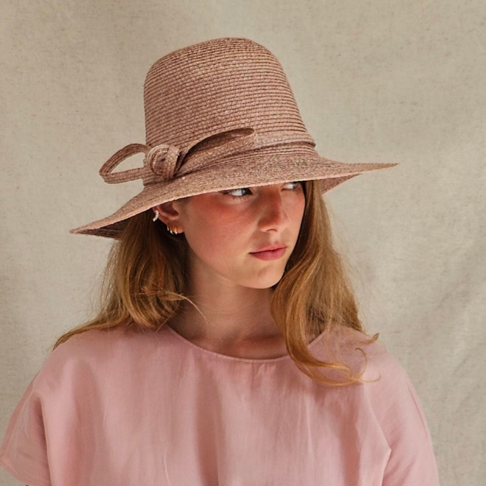 Pink straw sunhat with beautiful bow embellishment, side view.