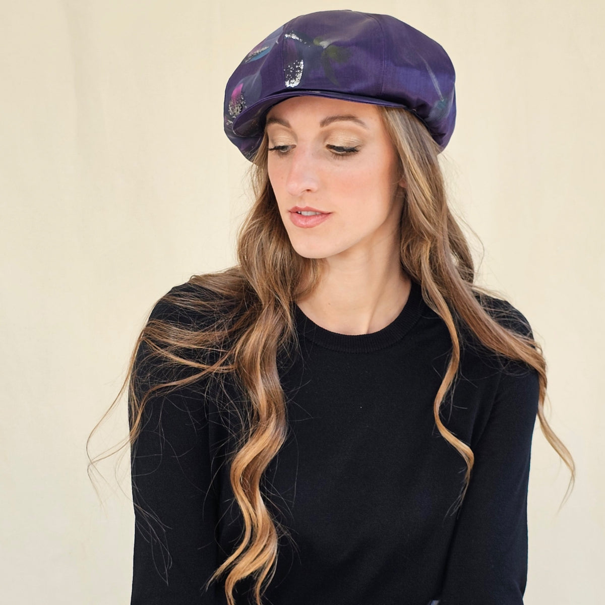 Purple hand-painted silk baker boy cap, angled view with model
looking down.
