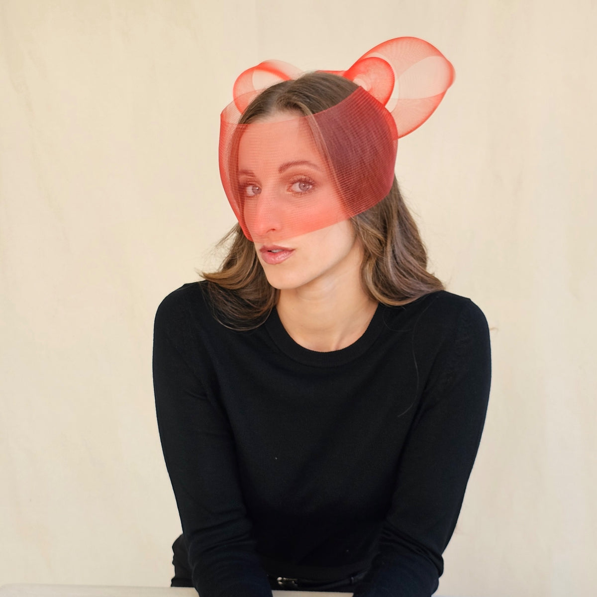 Angled view of red crin bow face veil on a seated model.