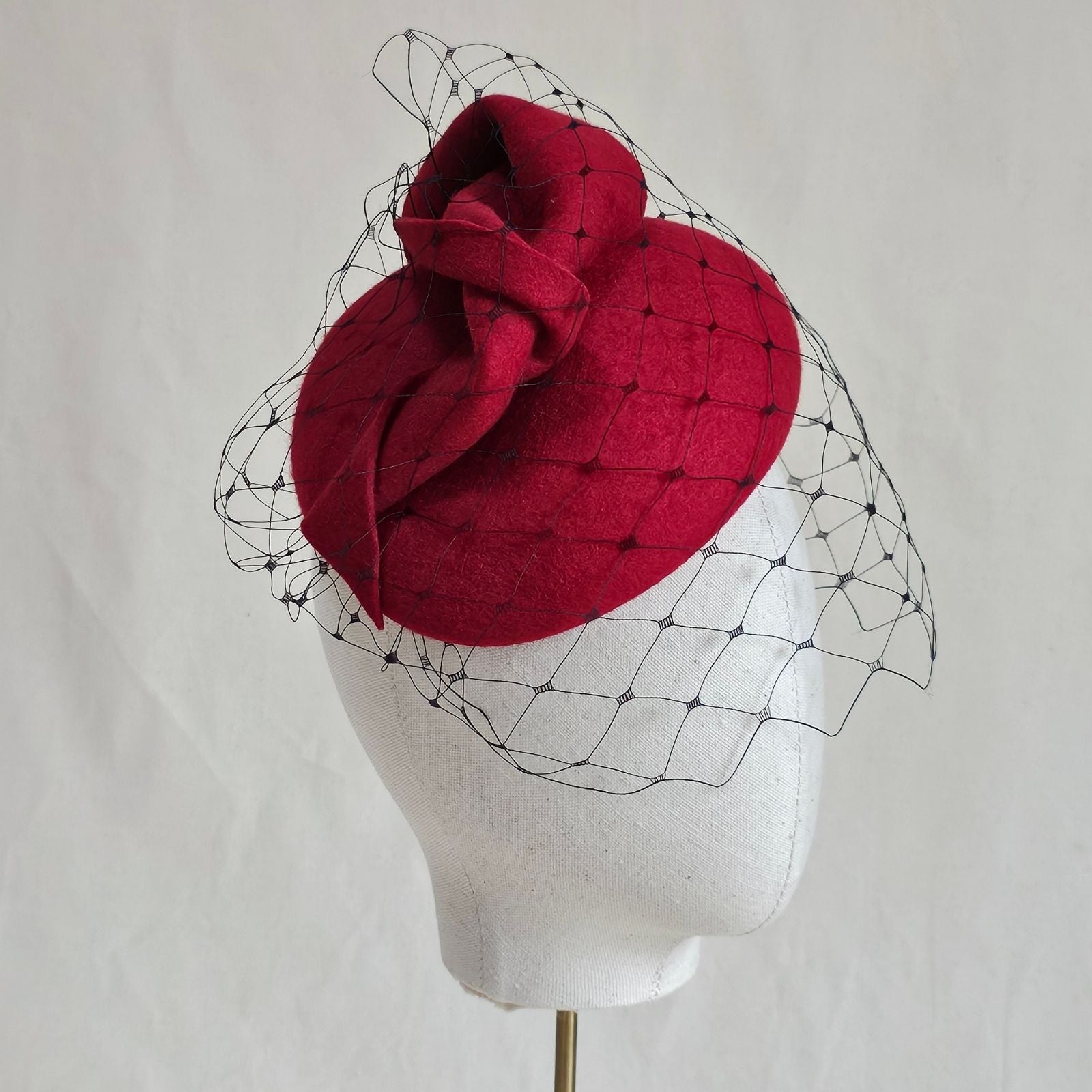 Red felt beret with dramatic twist and subtle veil, side view.