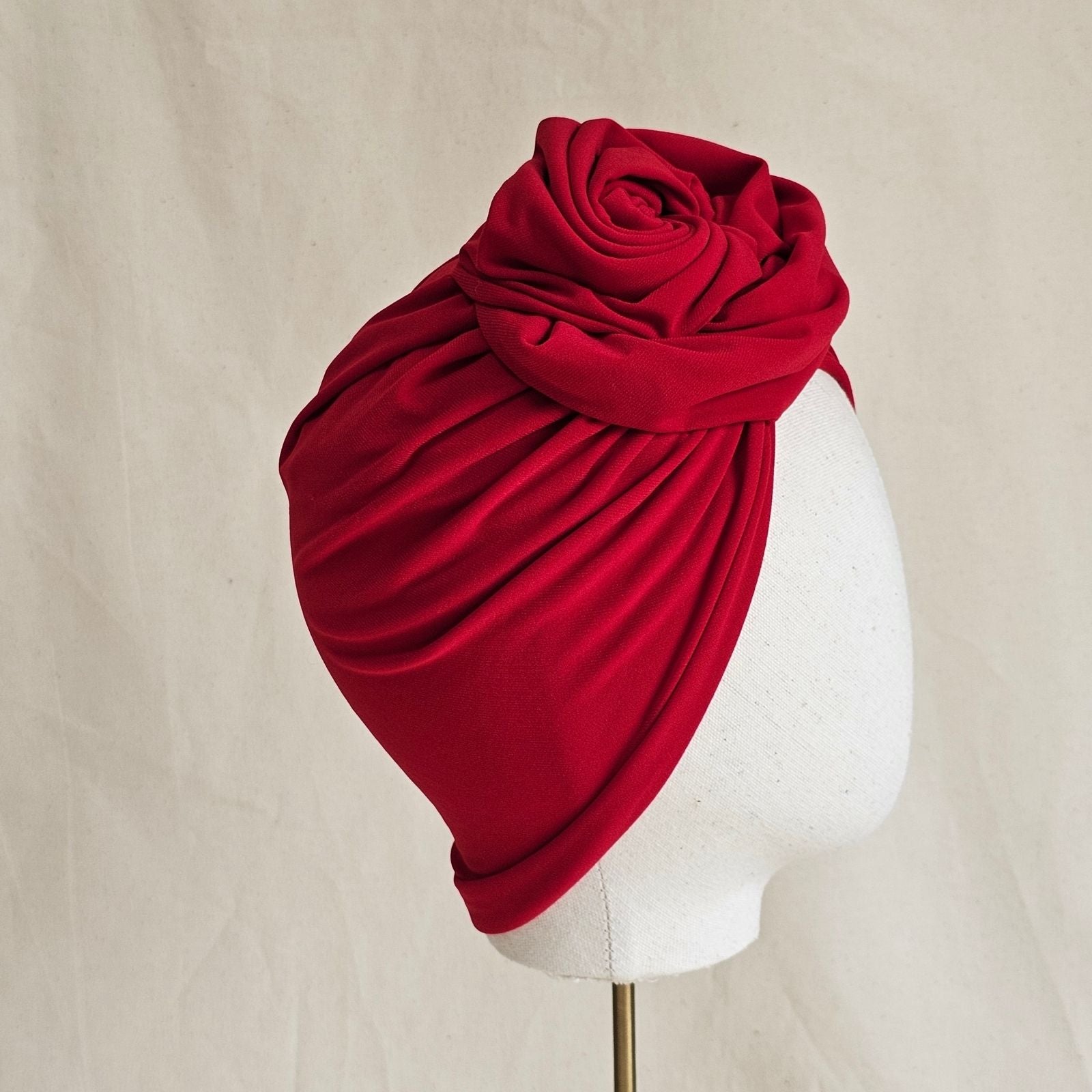 Red jersey turban gathered into sculpted intricate rose knot, side view.
