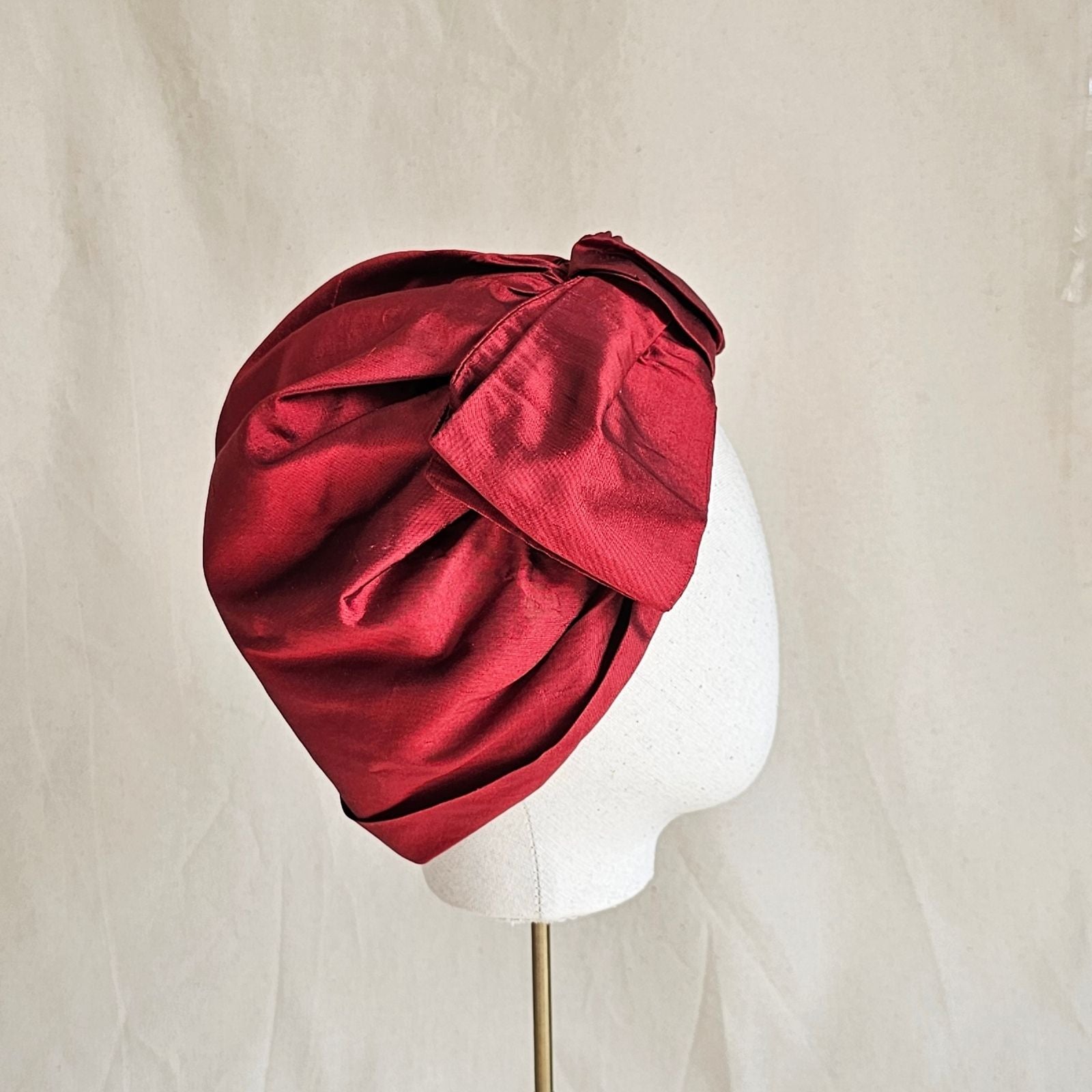 Red silk turban with bow embellishment, side view.