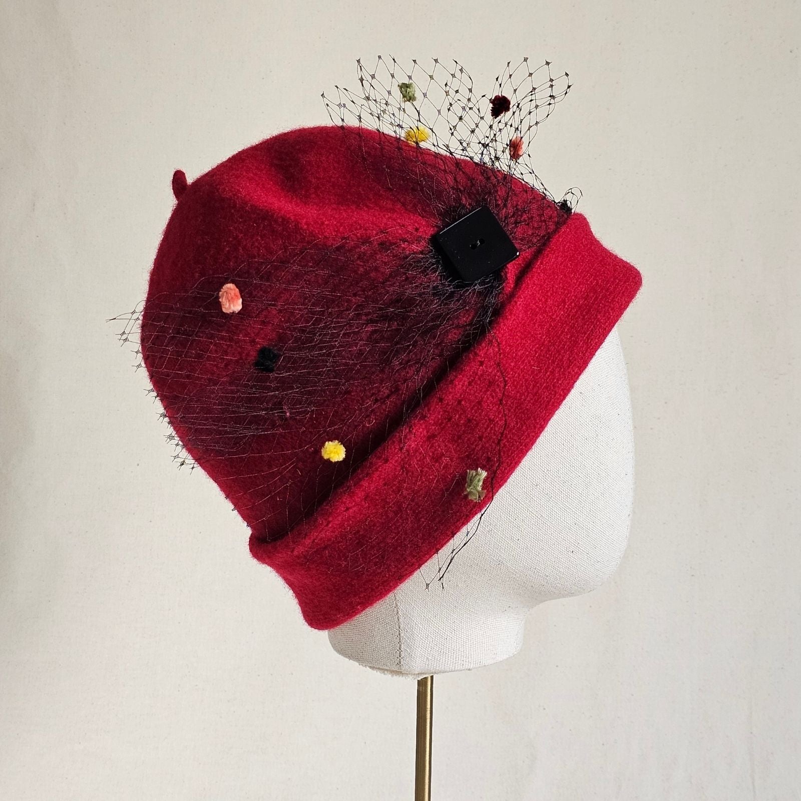 Red wool beanie with multicoloured spot veiling bow, side view.